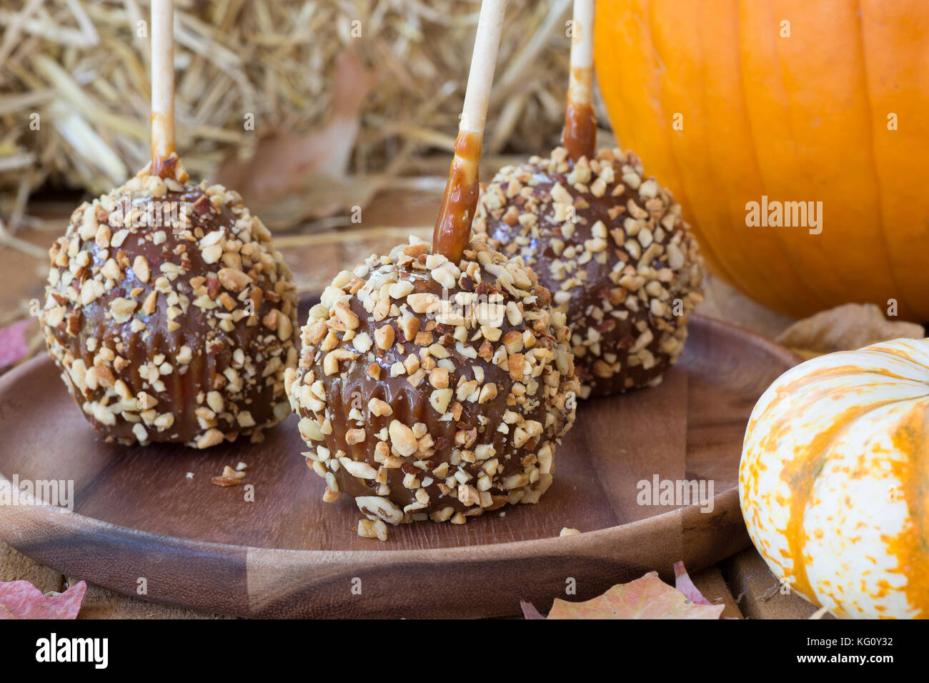 Caramello mele rivestite con i dadi su un piatto di legno con zucche Foto Stock