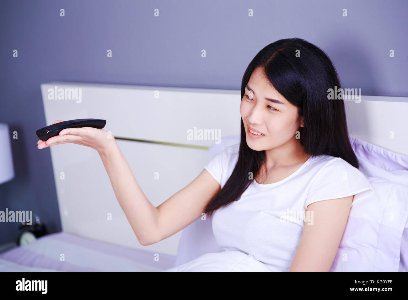 Smilling donna con il telecomando del televisore sul letto in camera da letto Foto Stock