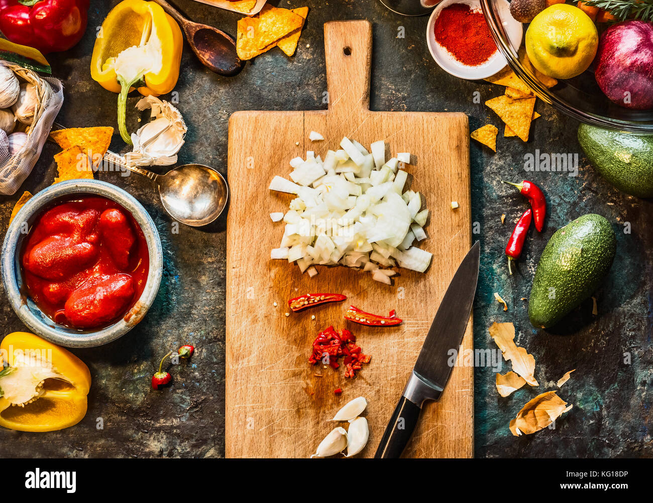 Spezie tritate sul tagliere di legno con coltello: peperoncino, cipolla e aglio con verdure ingredienti per cucina messicana on dark cucina rustica tab Foto Stock