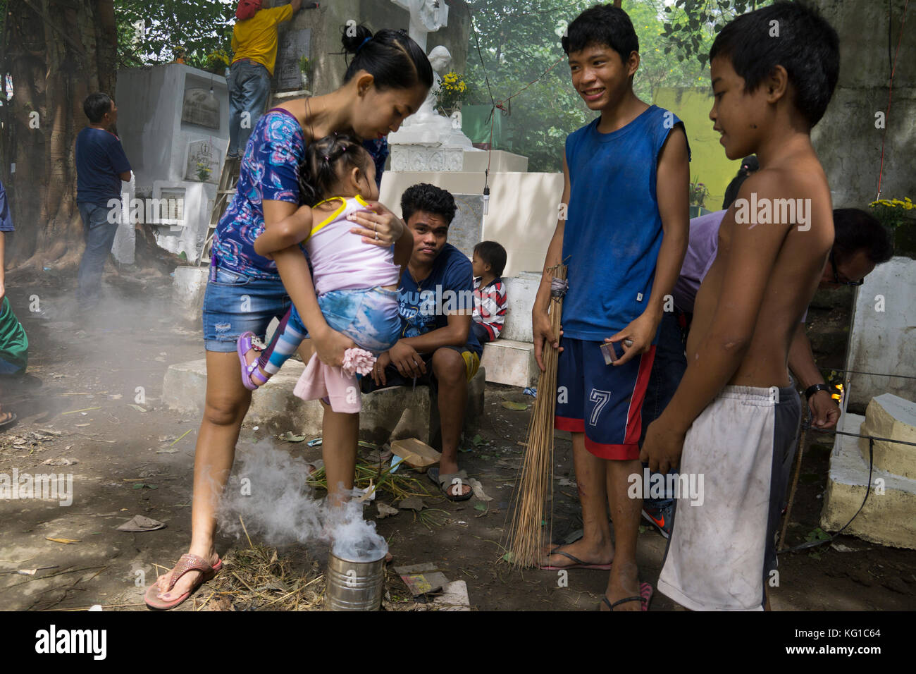 Veterans Cemetery, Cebu City, Filippine. 02 novembre 2017. All'interno dei cimiteri i bambini illuminano i fuochi che escudi fumo nella credenza che si cura fuori spiriti malvagi.qui una madre passa attraverso il fumo con il suo bambino piccolo. Credit: Imagegallery2/Alamy Live News Foto Stock