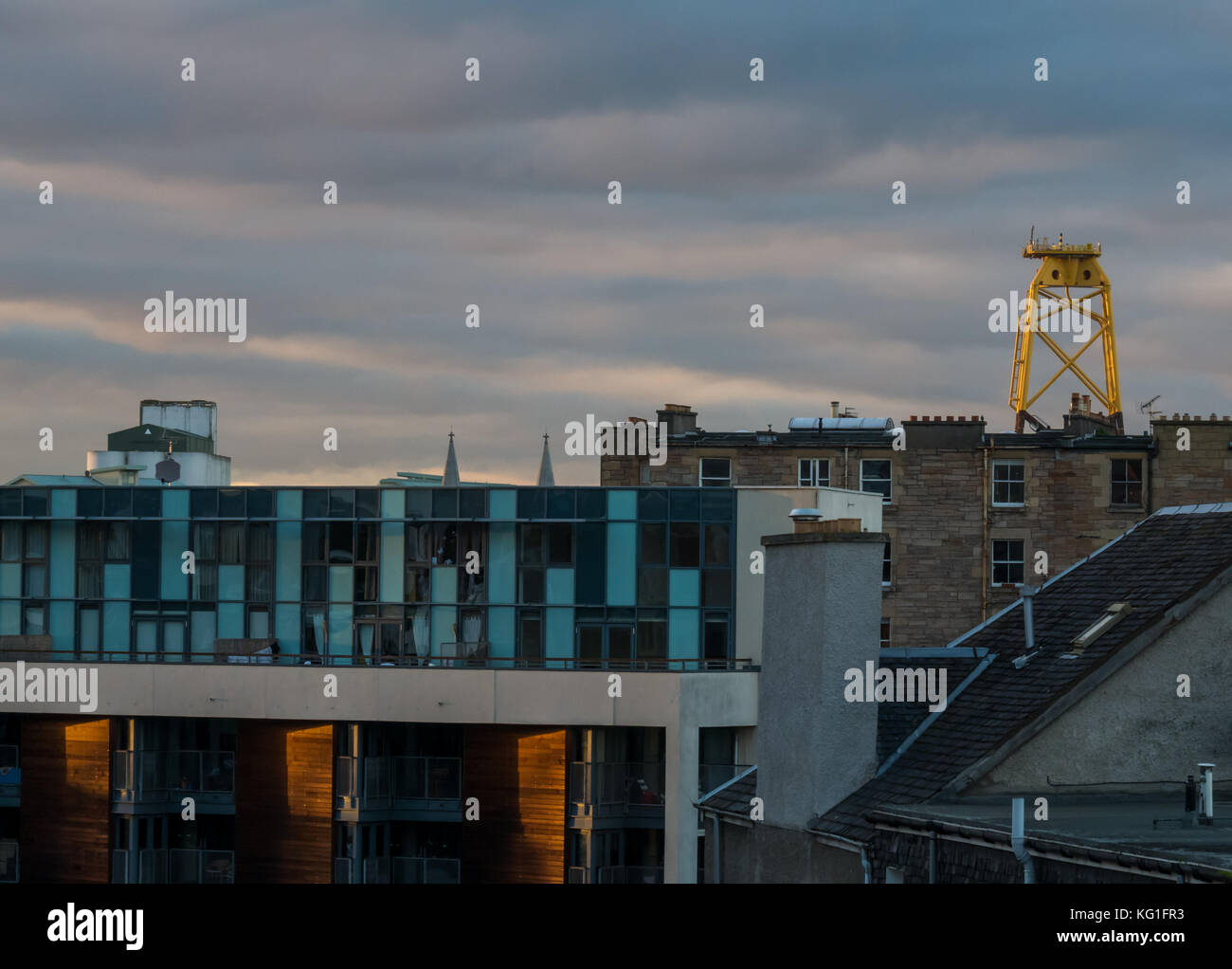 Leith, Edimburgo, Scozia, Regno Unito. Bassa pomeriggio di sole sopra i tetti in Leith, con alte giallo turbina eolica platform torreggianti sull orizzonte, appena prima del tramonto Foto Stock