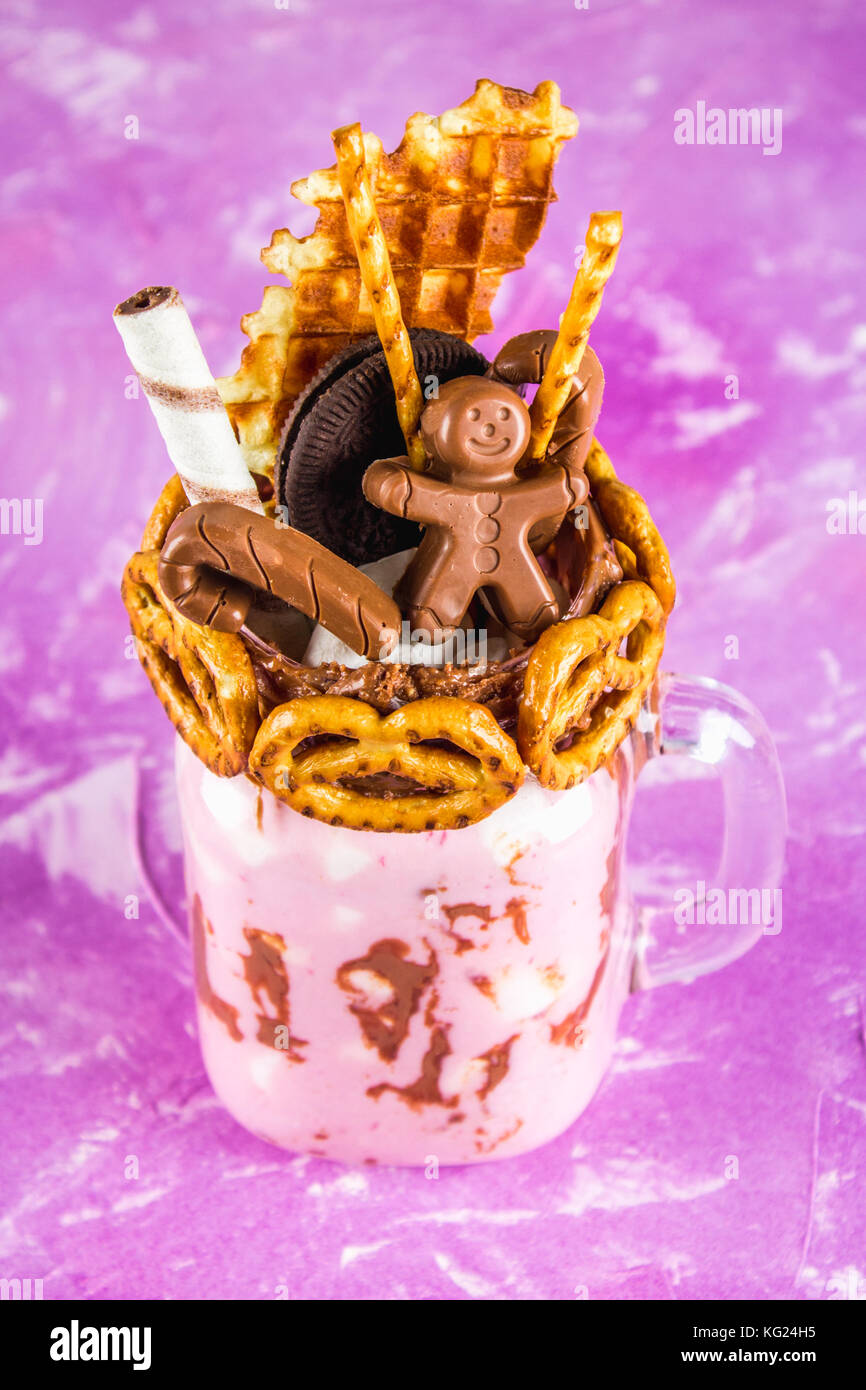 Freakshake dal frullato di rosa, crema. monstershake con un uomo di cioccolato, di canna da zucchero, salatini, biscotti, cialde e marshmallow. extreme frullato in un mas Foto Stock