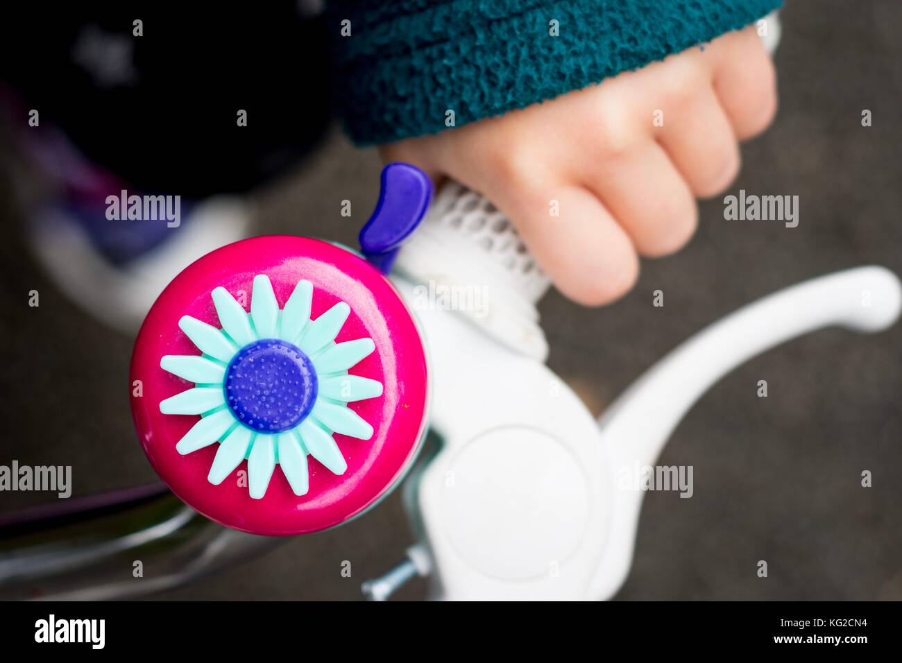 Bambino la mano che impugna il manubrio di una bicicletta. Campana rosa decorata con un fiore. Rimrose Valley Park, Sefton, Liverpool, Merseyside. Foto Stock