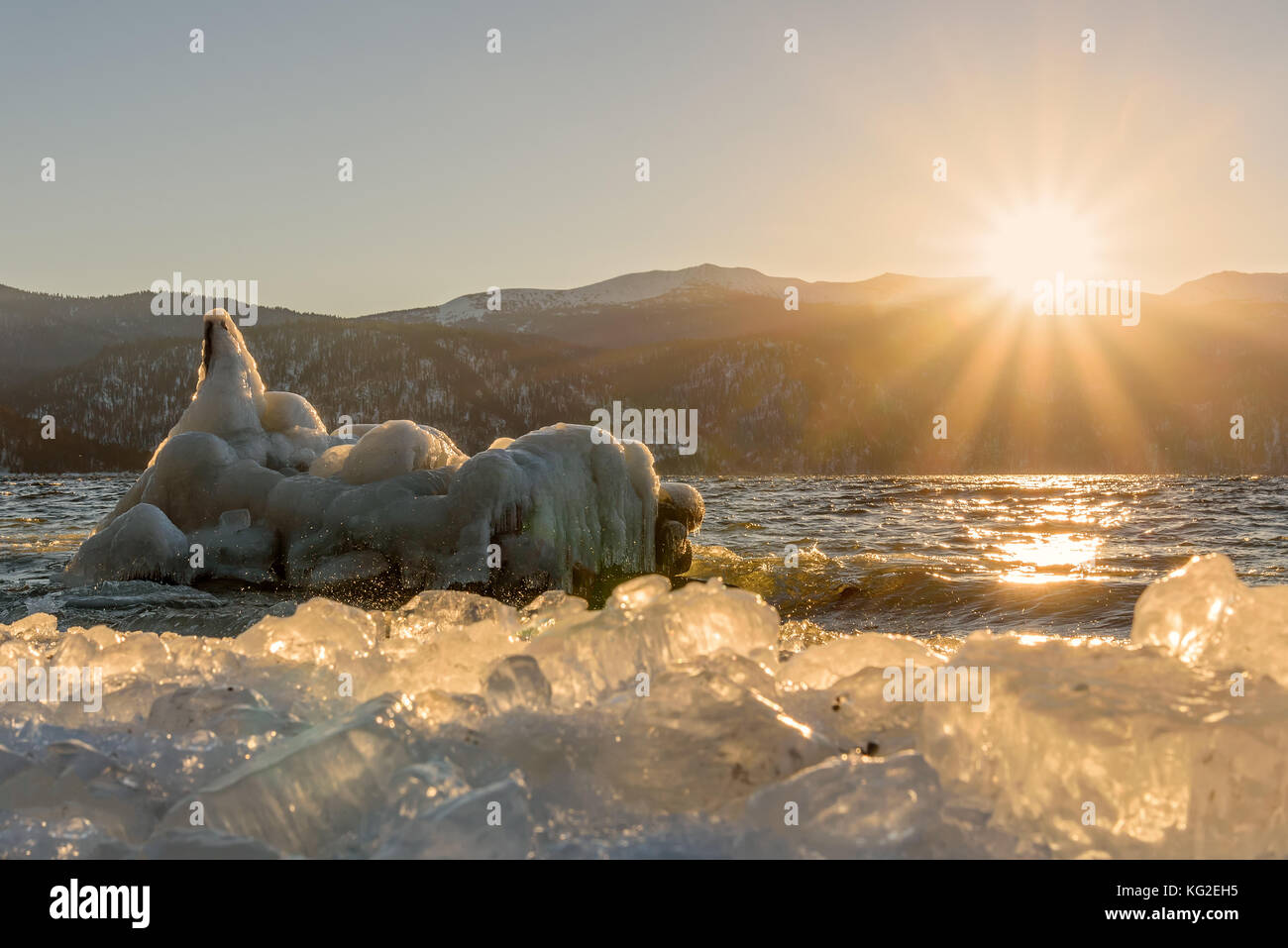 Incantevole paesaggio invernale con un lago, il sole, iceberg su acqua e ghiaccio sulla banca sullo sfondo di montagne all'alba Foto Stock