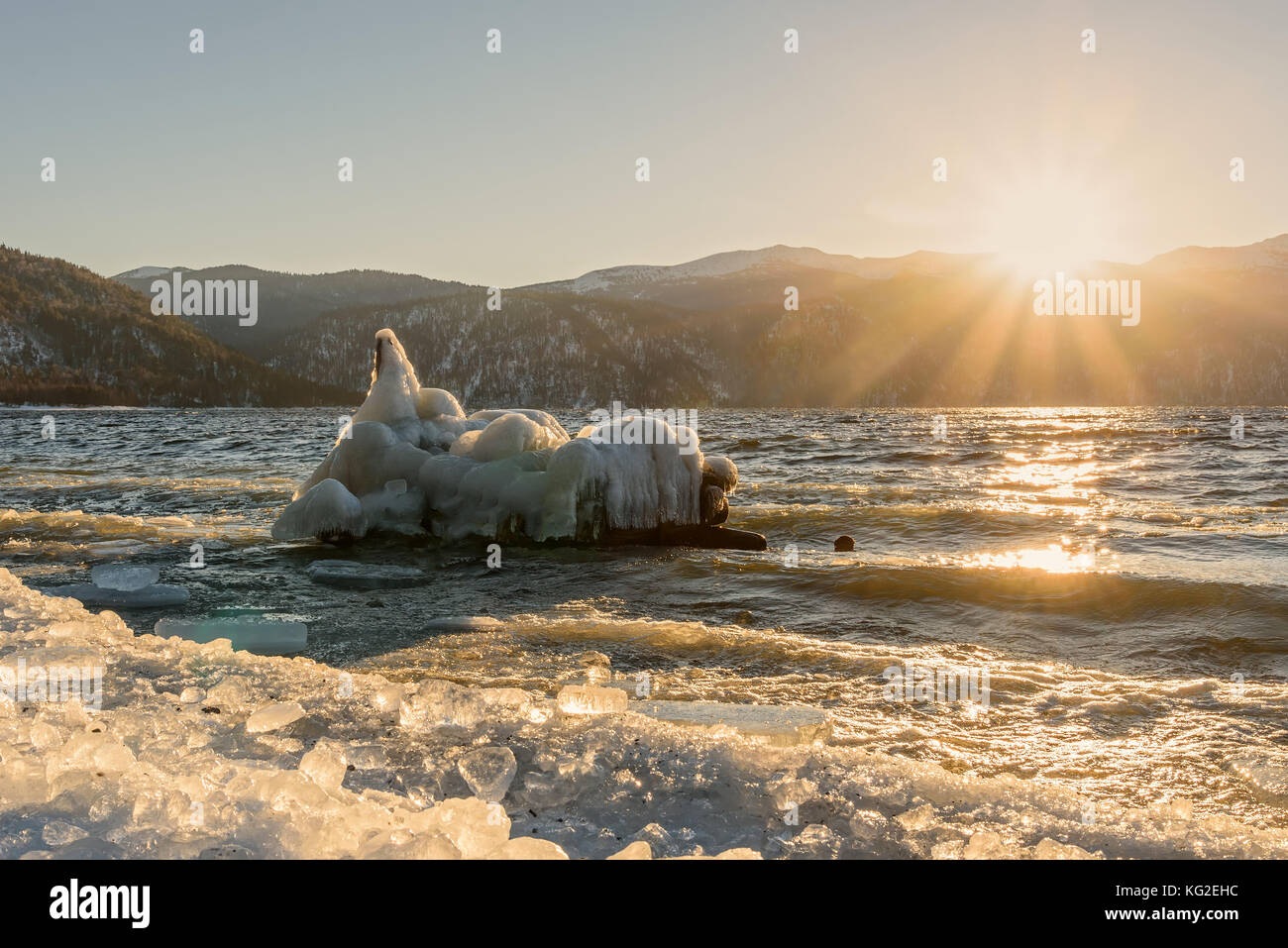 Incantevole paesaggio invernale con un lago, il sole, iceberg su acqua e ghiaccio sulla banca sullo sfondo di montagne all'alba Foto Stock