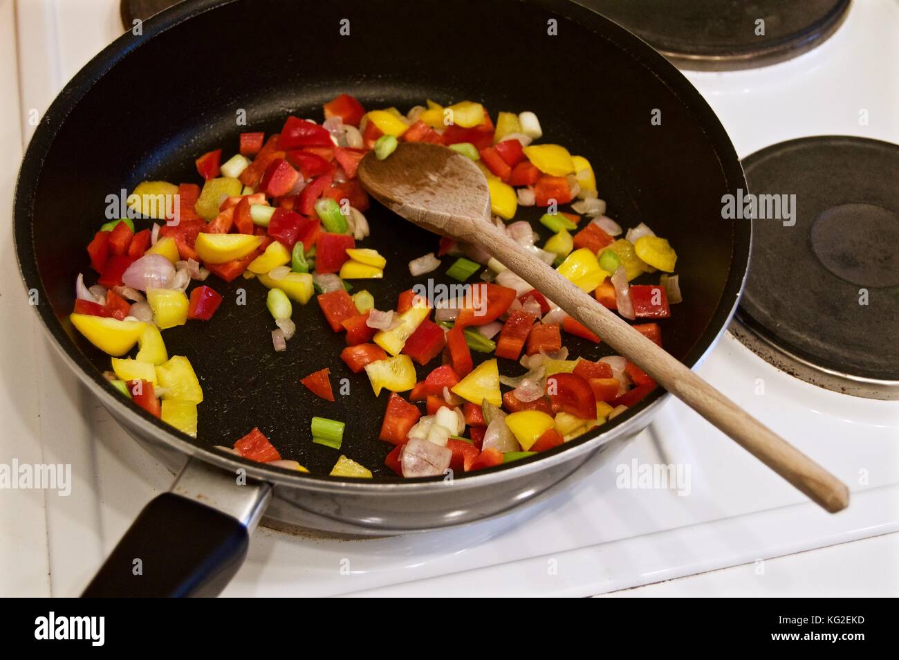 La cottura di una paella sul piano di cottura in un rivestito in teflon wok con il cucchiaio di legno Foto Stock