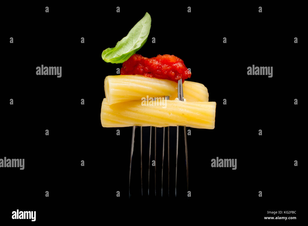 La pasta in sfondo nero. rigatoni, pomodoro e basilico sulla forcella. cucina italiana concept Foto Stock