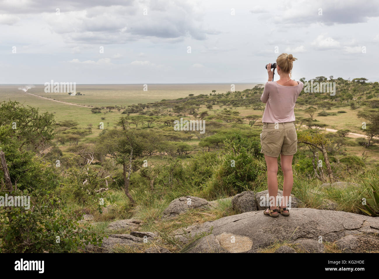 Turista femminile guardando attraverso il binocolo su african safari nel Serengeti National Park. tanzania, afrika. Foto Stock
