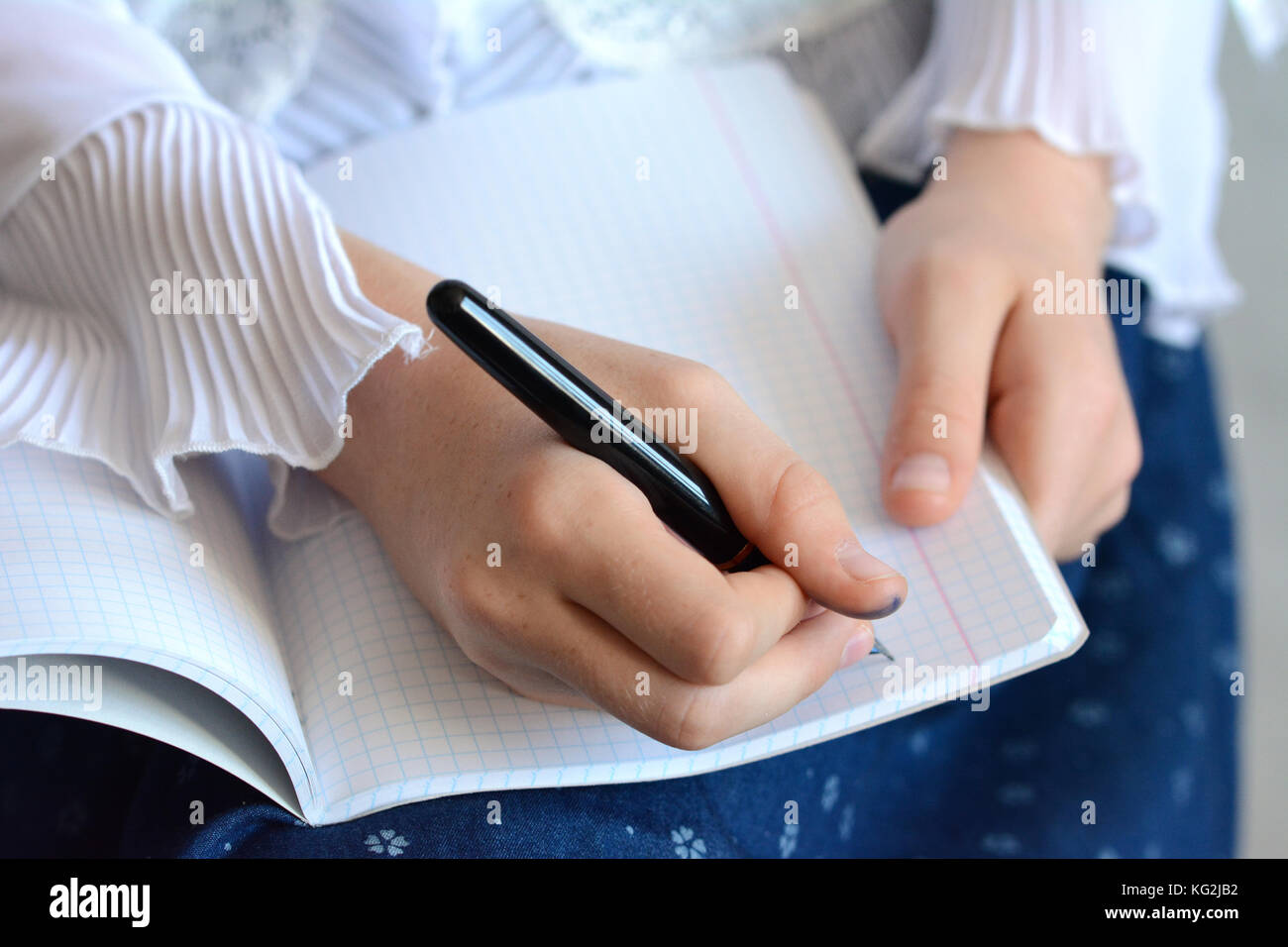 Primo giorno di scuola - una ragazza che indossa una camicia bianca e un blu scuro mantello iscritto nel suo notebook Foto Stock