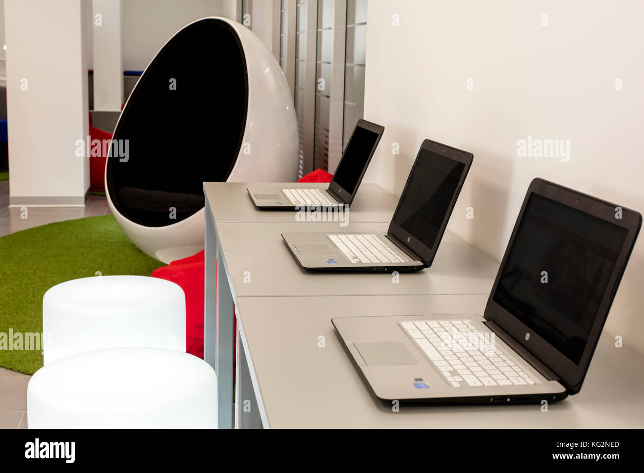 Ufficio moderno con fila di lap-top; uova a forma di sedia in background. Foto Stock