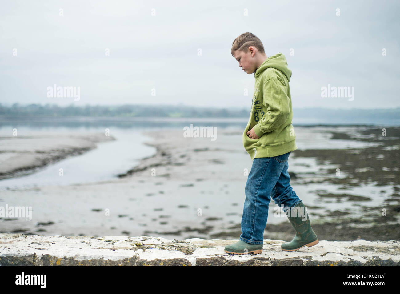 Giovedì 02 Novembre 2017 Una giovane 8,9,10 anno vecchio ragazzo passeggiate lungo una parete verde da indossare gli stivali da pioggia Foto Stock
