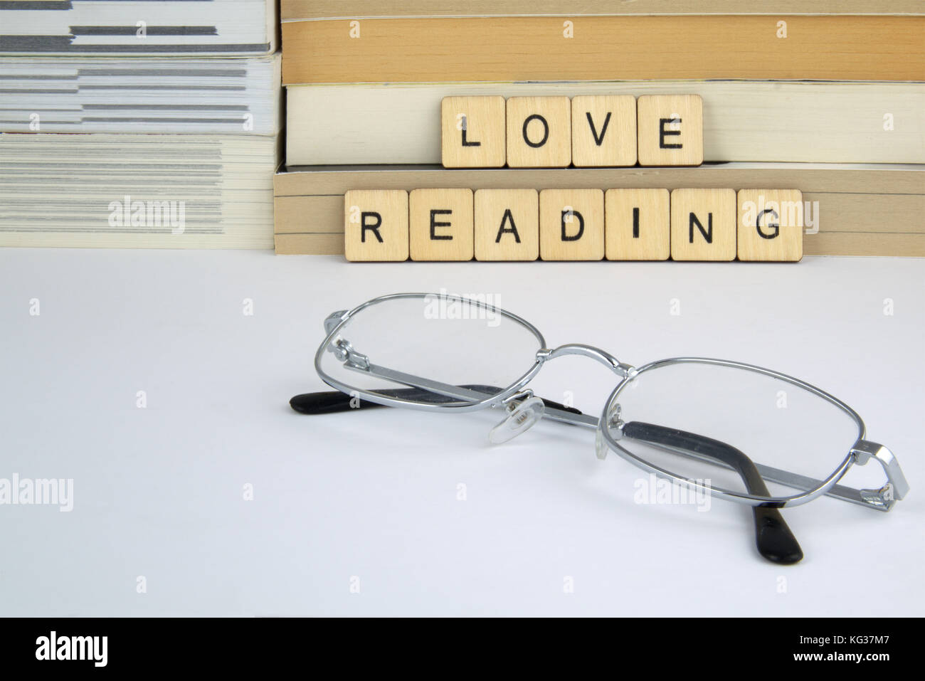Le parole amare la lettura scritto nella lettera di piastrelle in appoggio contro una pila di libri e romanzi su una superficie bianca con alcuni bicchieri d'argento (occhiali) Foto Stock