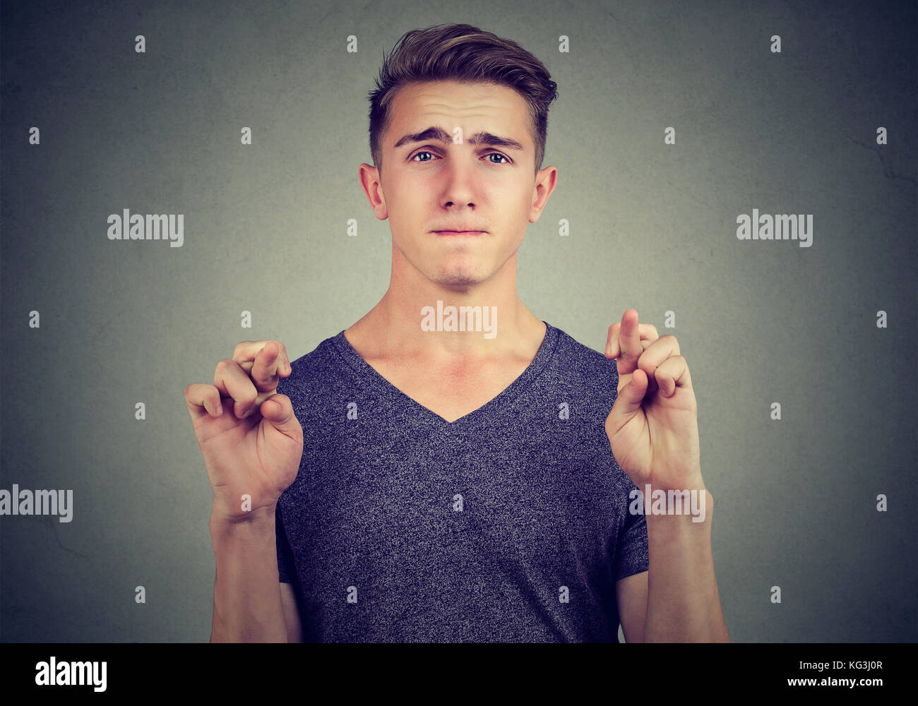 Uomo di speranza incrocio le dita sperando isolato sul muro grigio Sfondo. le emozioni umane, sentimenti reazione Foto Stock