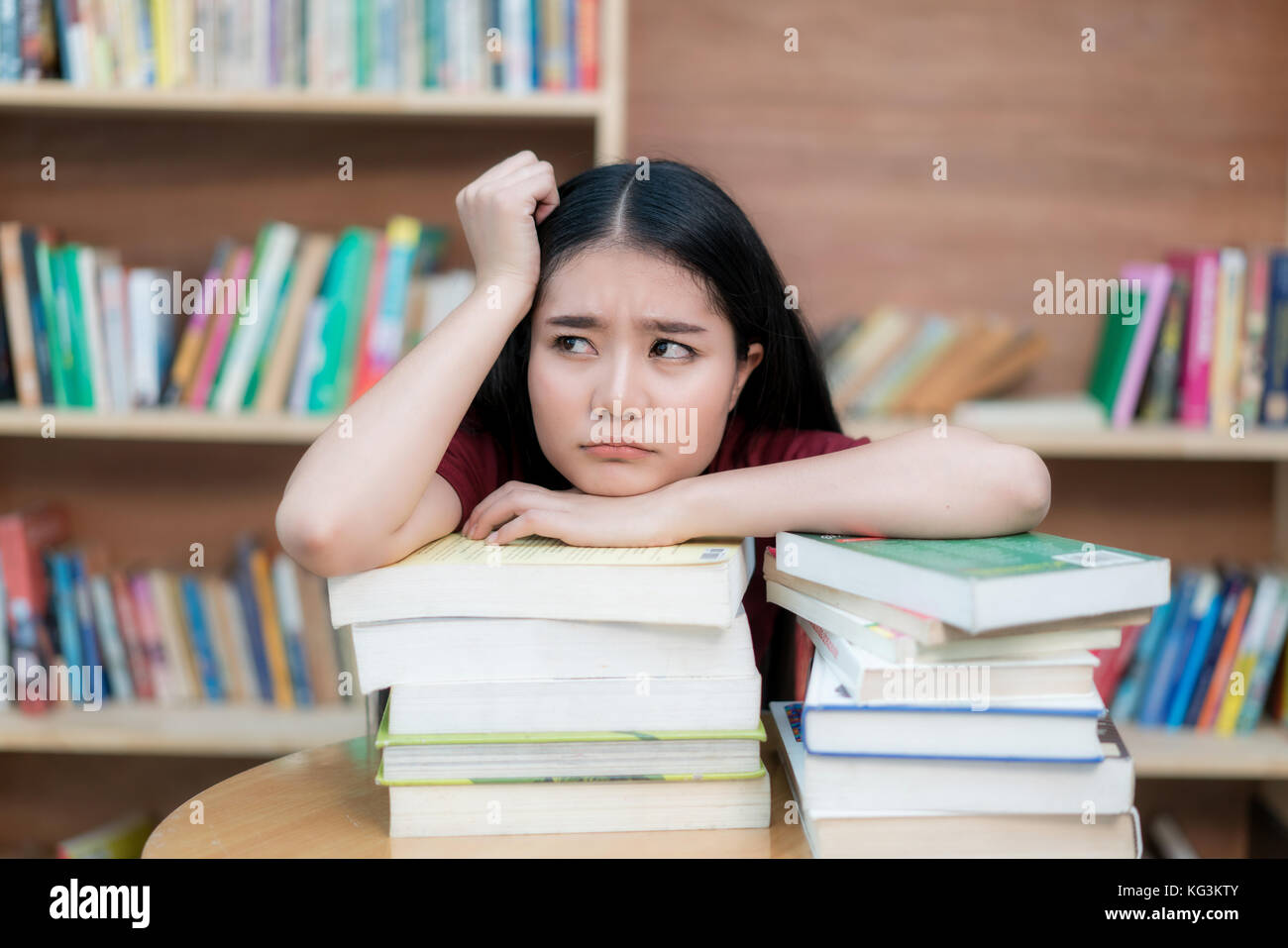 Donna asiatica studente noioso libro di lettura in biblioteca con un sacco di libri in università. Asian studente sfiduciato libro di lettura per l'esame. Foto Stock