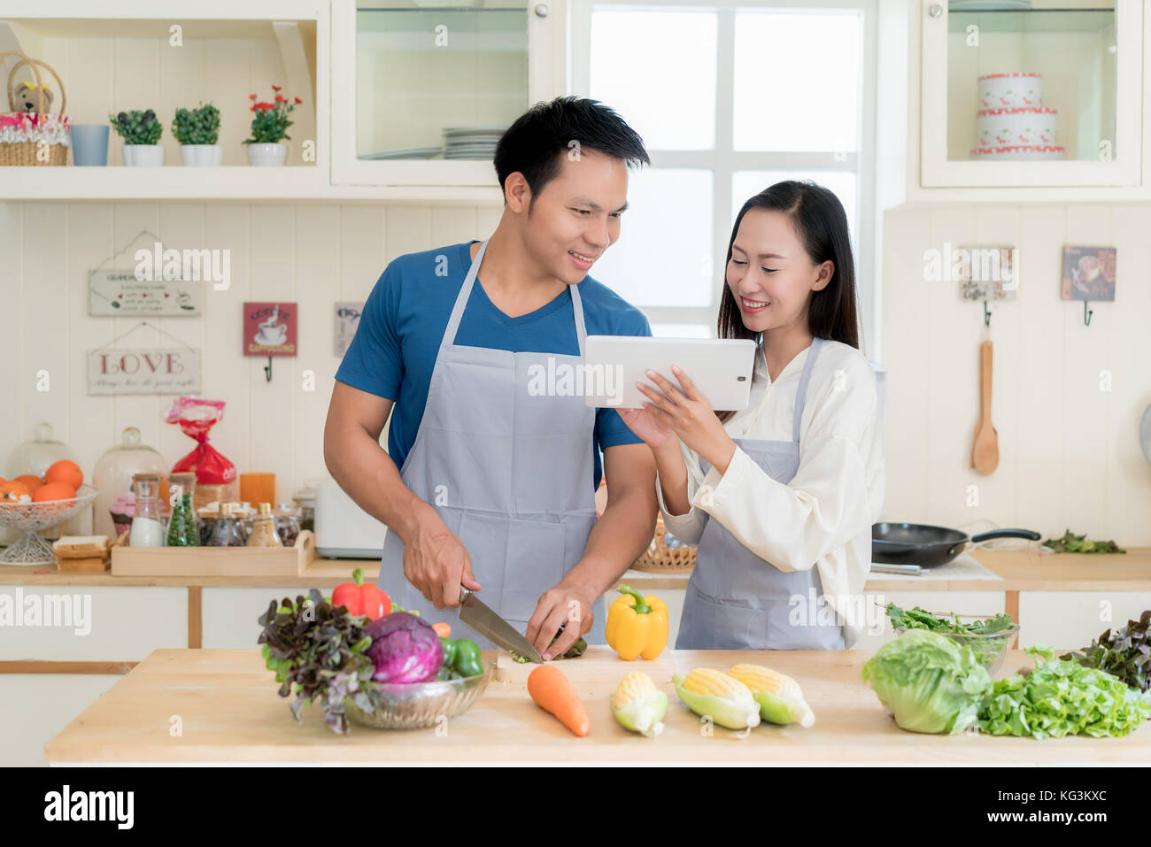 Asian giovane e bella moglie e marito menu ricerca ricetta in digitale compressa nella cucina di casa. felice amore giovane e concetto tecnologico. Foto Stock