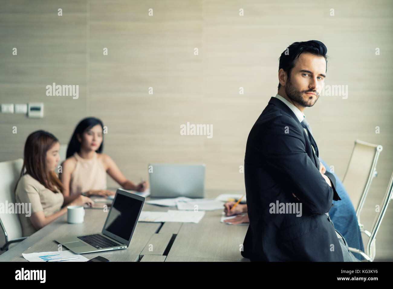 Happy business man in piedi con le braccia incrociate in ufficio mentre i colleghi a discutere in background. Foto Stock