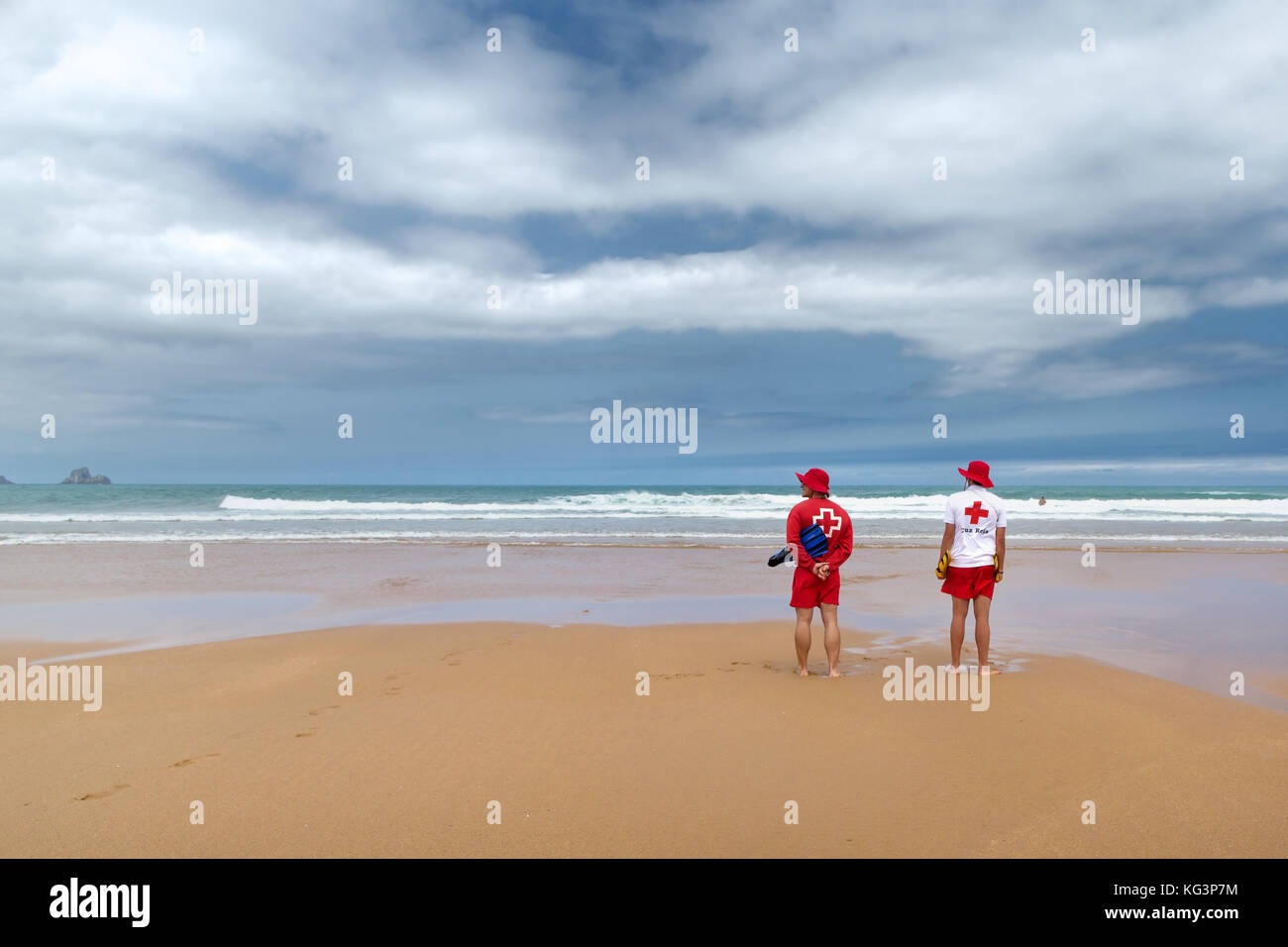 Orinon, Spagna - luglio 6, 2016: due soccorritori sconosciuto sulla deserta spiaggia sabbiosa. soccorritori in rosso-bianco appendiabiti di fronte all'oceano. in onde il sai Foto Stock