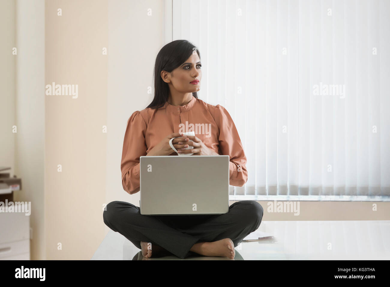 Imprenditrice con caffè utilizzando laptop seduto sulla scrivania Foto Stock