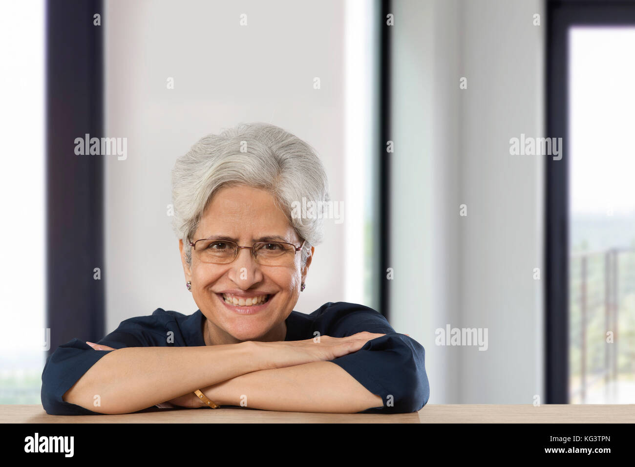 Felice senior donna appoggiata sul tavolo con le braccia incrociate Foto Stock