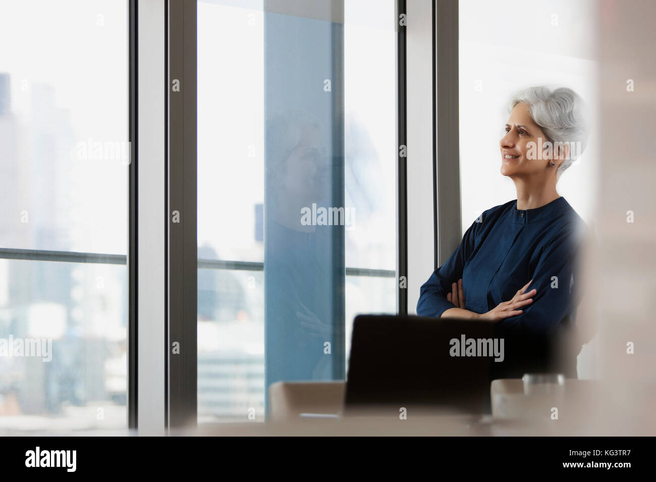 Felice senior donna seduta con le braccia incrociate in poltrona a casa Foto Stock