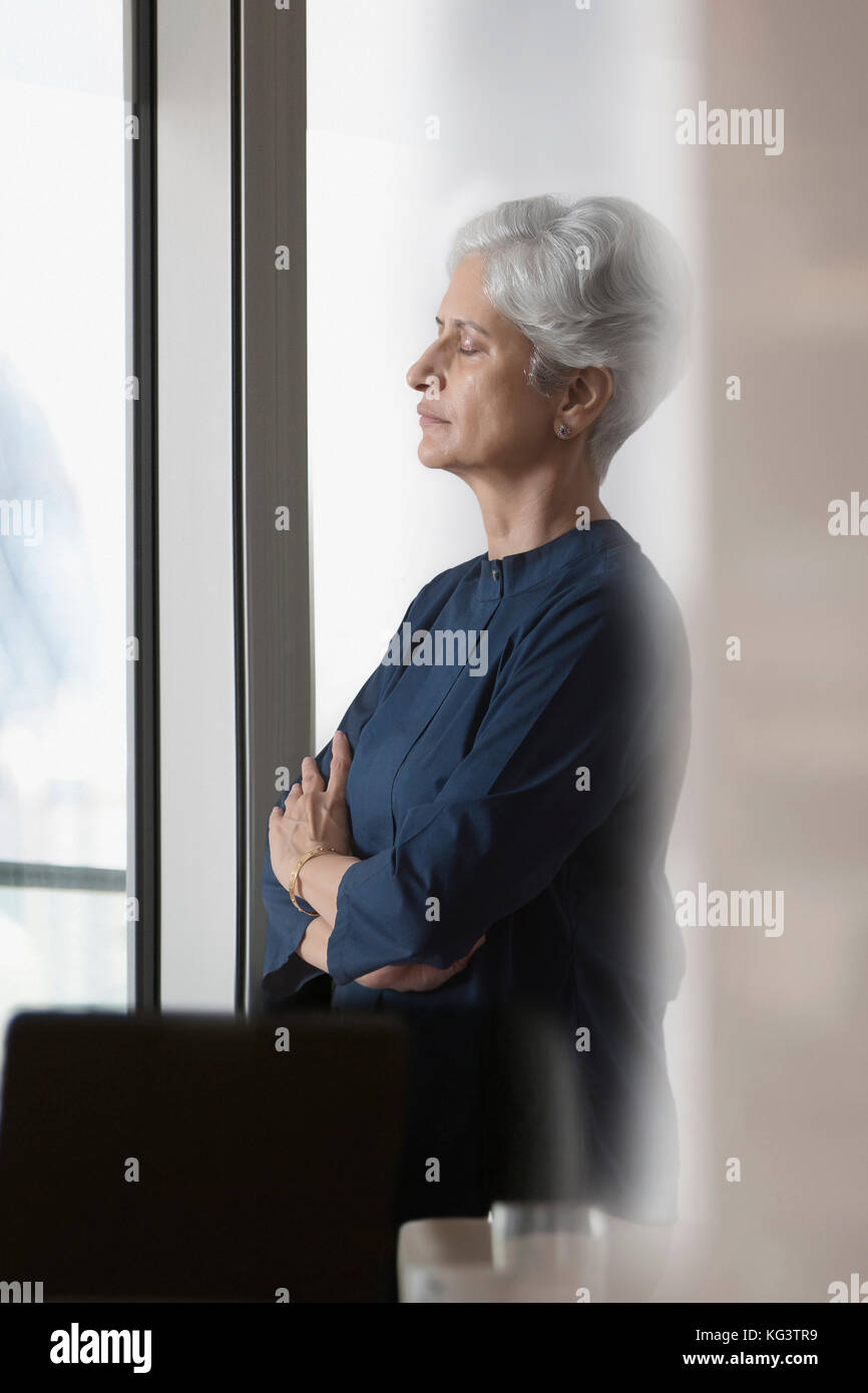 Senior woman standing gli occhi chiusi vicino a finestra Foto Stock