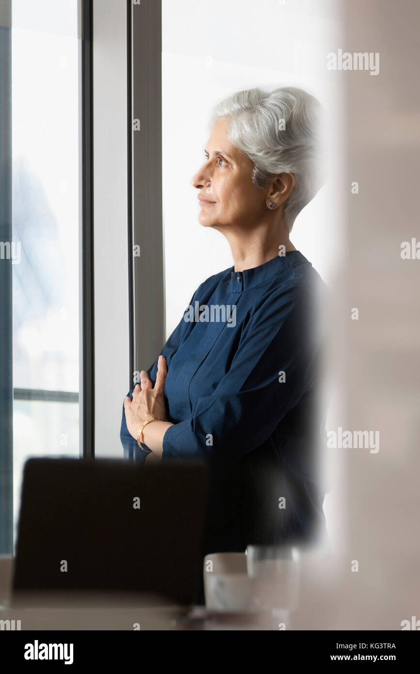Senior donna in piedi vicino alla finestra Foto Stock