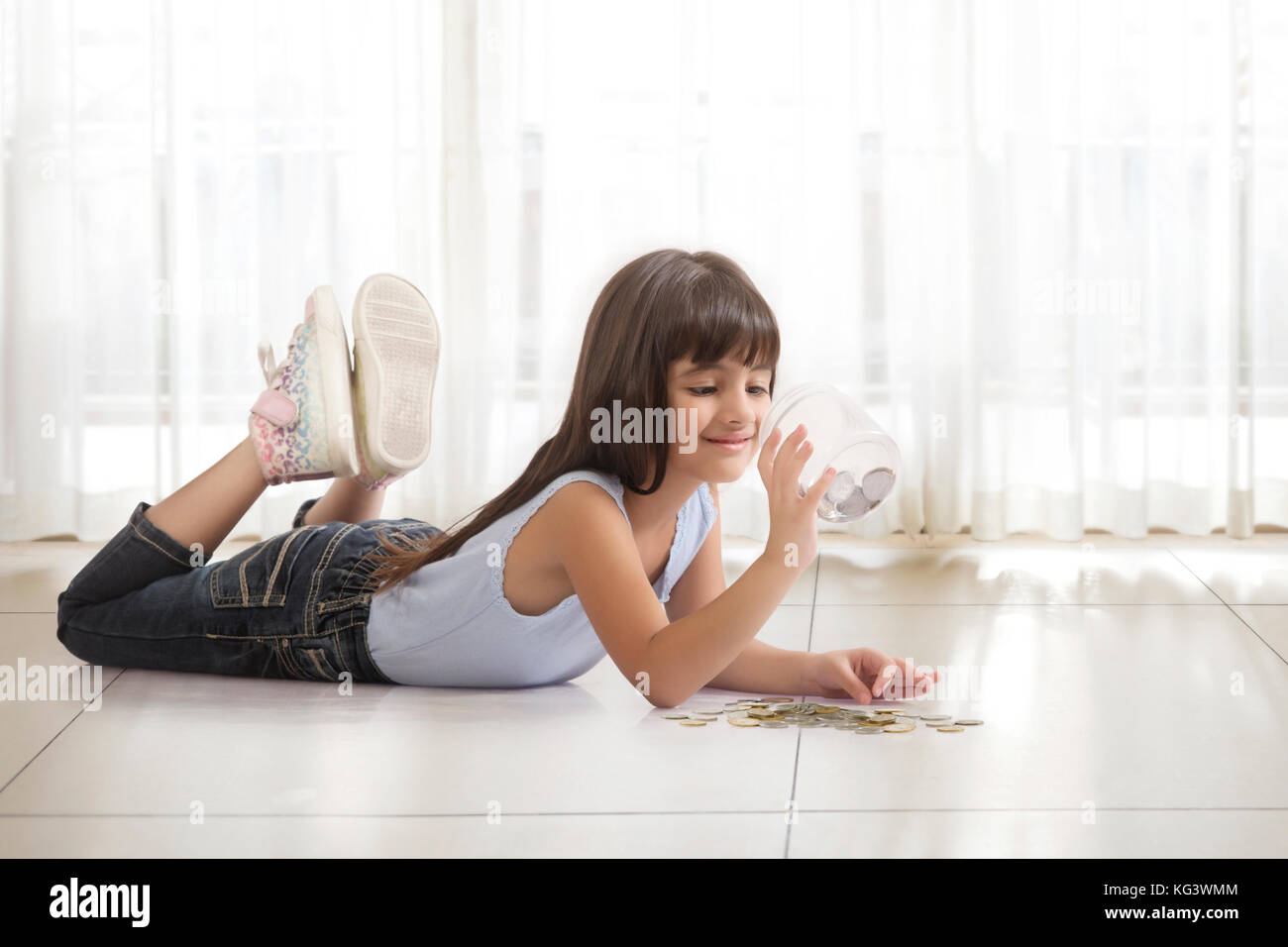 Bambina giacente sul piano cercando nella casella di denaro Foto Stock