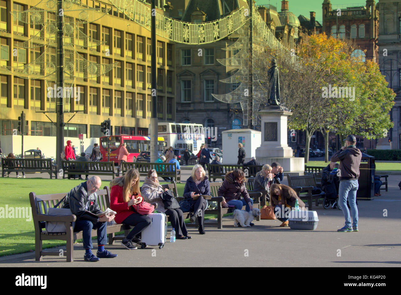 La gente del posto e i turisti godetevi il tardo sole seduti sui sedili panche George Square, Glasgow city, Regno Unito Foto Stock