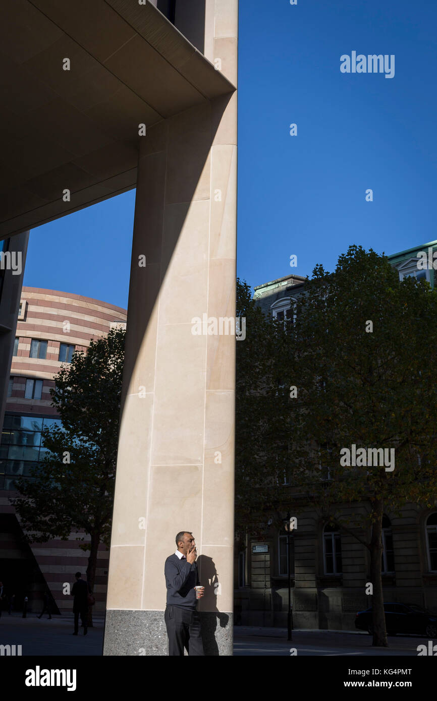 Un lavoratore della città prende un trascinamento sulla sua sigaretta permanente, mentre in autunno il sole al di fuori del nuovo Bloomberg uffici a Cannon Street, il 27 ottobre 2017, nella città di Londra, Inghilterra. Foto Stock