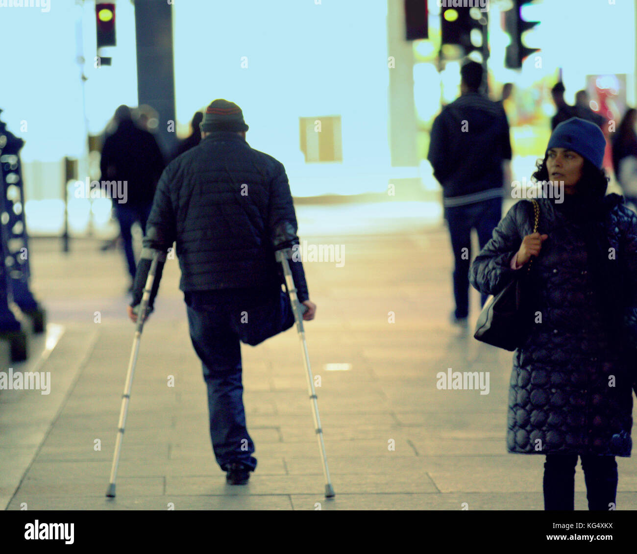 Zampe di un uomo con le stampelle camminando sulla strada vista da dietro Foto Stock