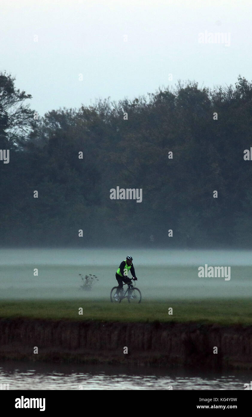 Un ciclista corre nella nebbia vicino Eton, Berkshire, dopo Londra e il sud-est ha avuto un MET Office giallo avvertimento di nebbia emesso ieri notte. Foto Stock