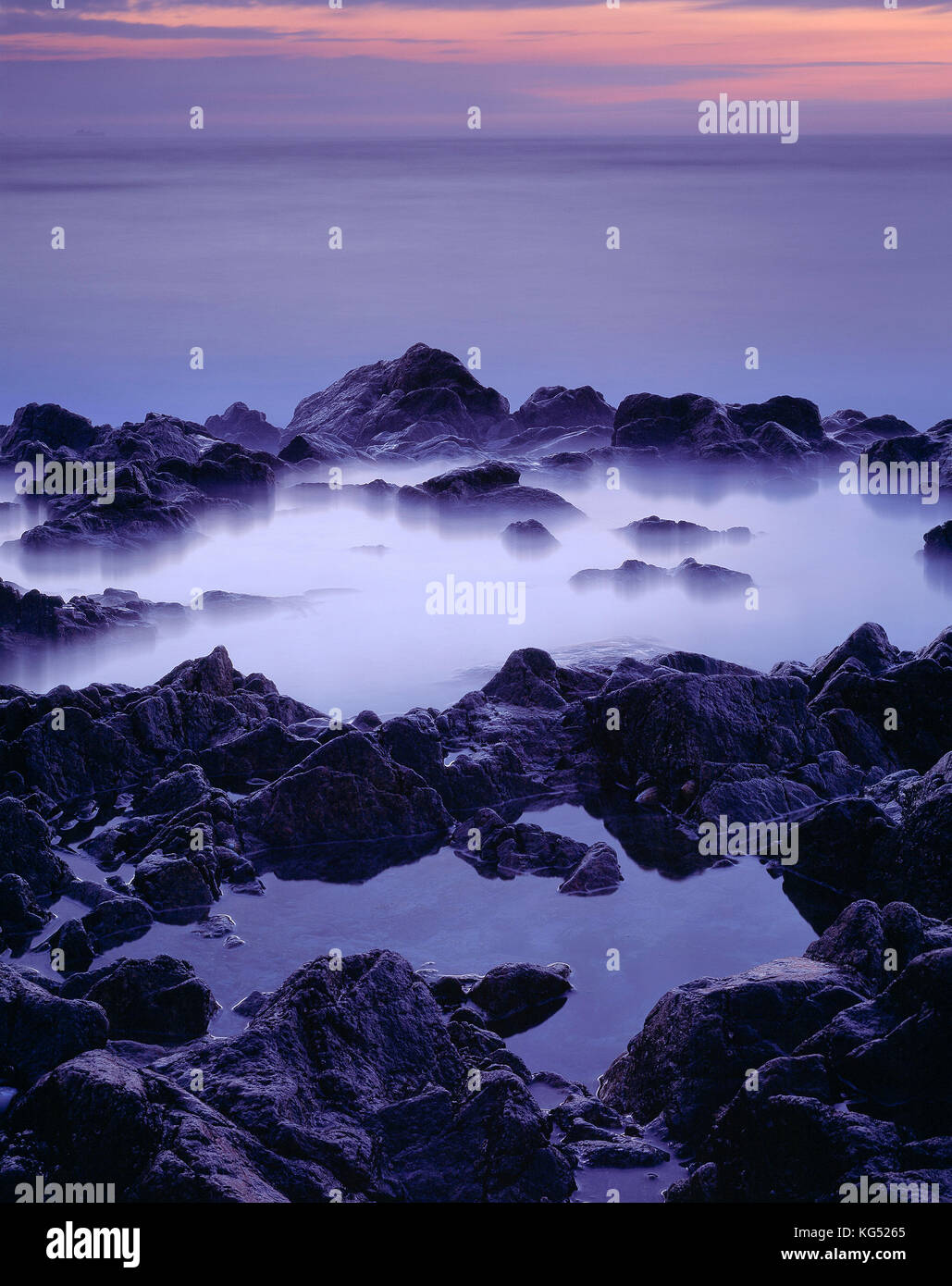 Isole del Canale. Guernsey. Coast close up misty piscine di roccia al tramonto. Foto Stock