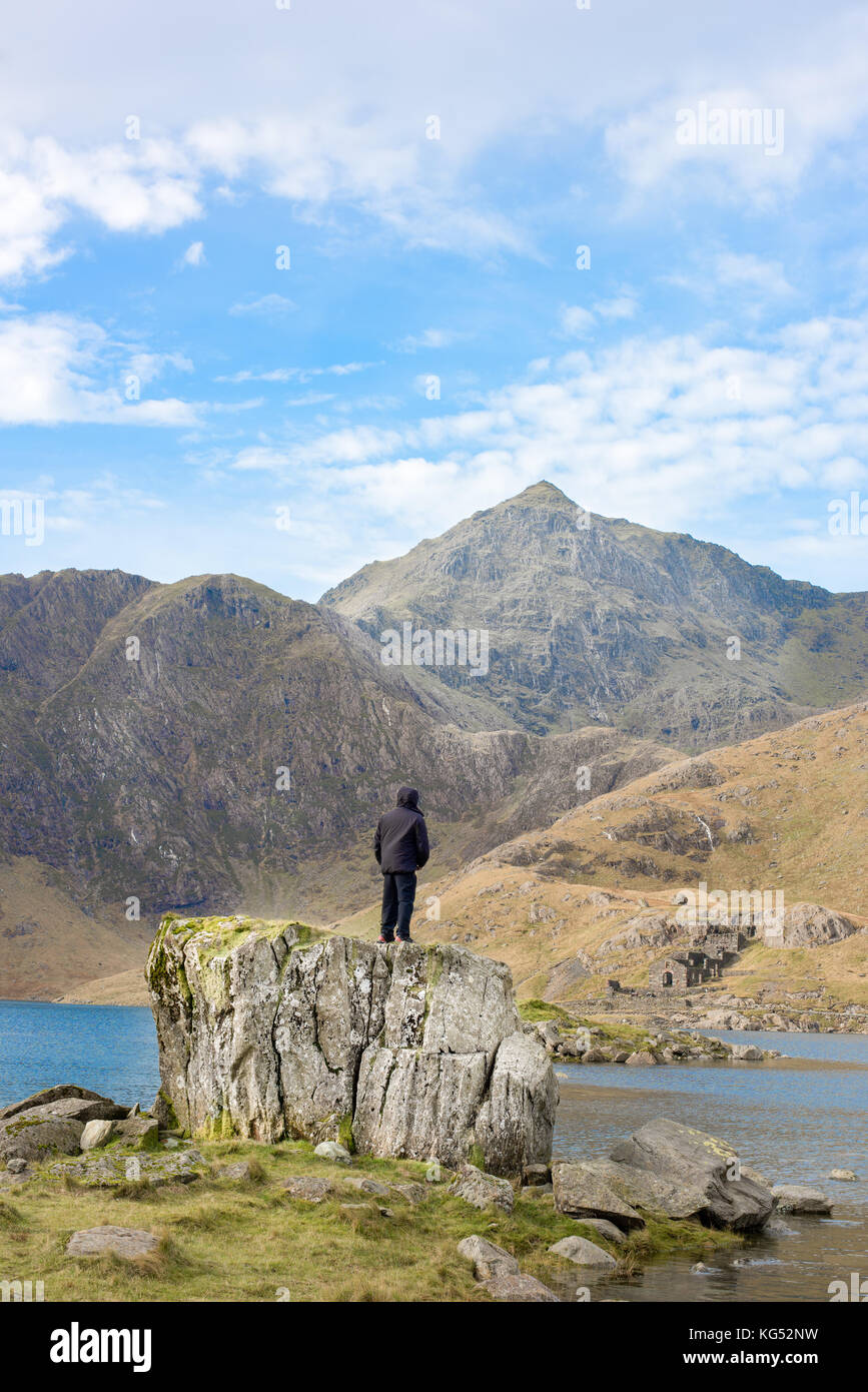 Uomo solitario sorge su una roccia e sguardi al picco di Mount Snowdon, la montagna più alta in Inghilterra e nel Galles. Foto Stock