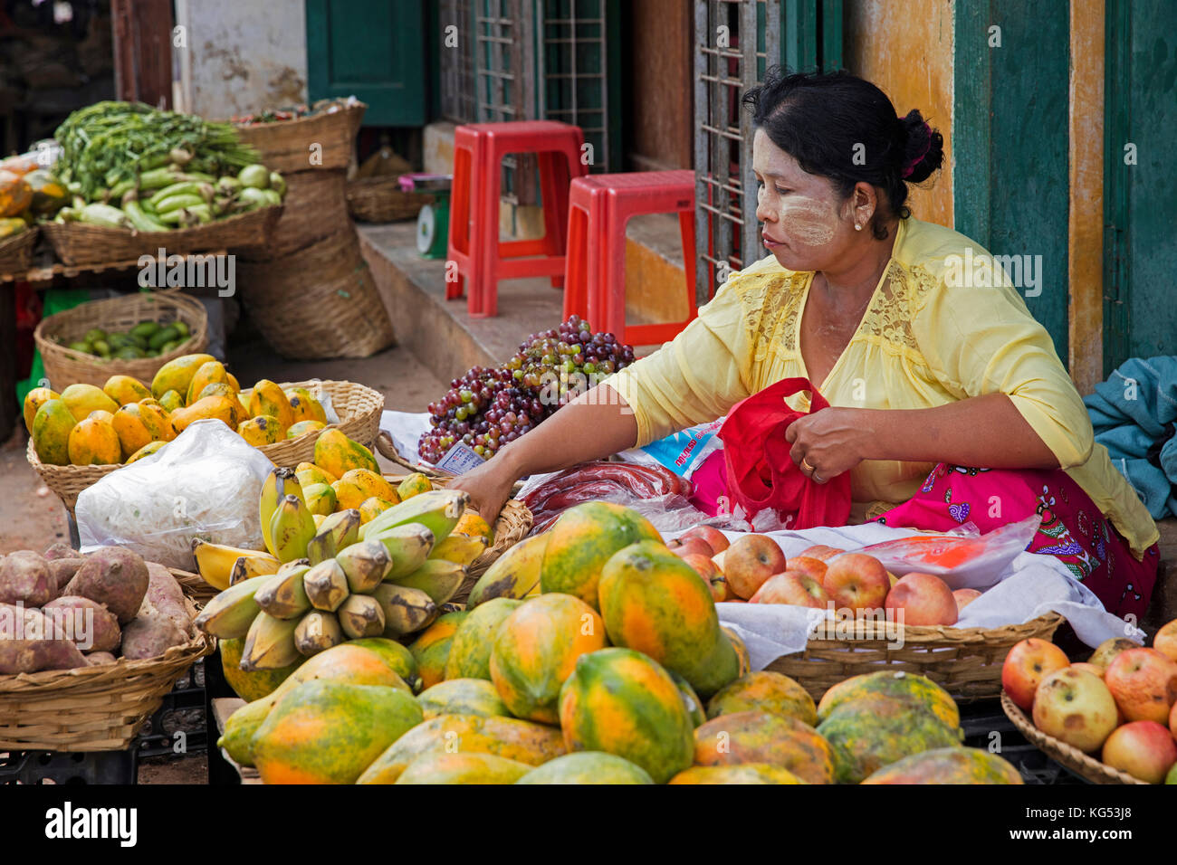 Donna birmano per la vendita di frutta, papaia e banane e mele al mercato alimentare nella città mandalay, myanmar / BIRMANIA Foto Stock
