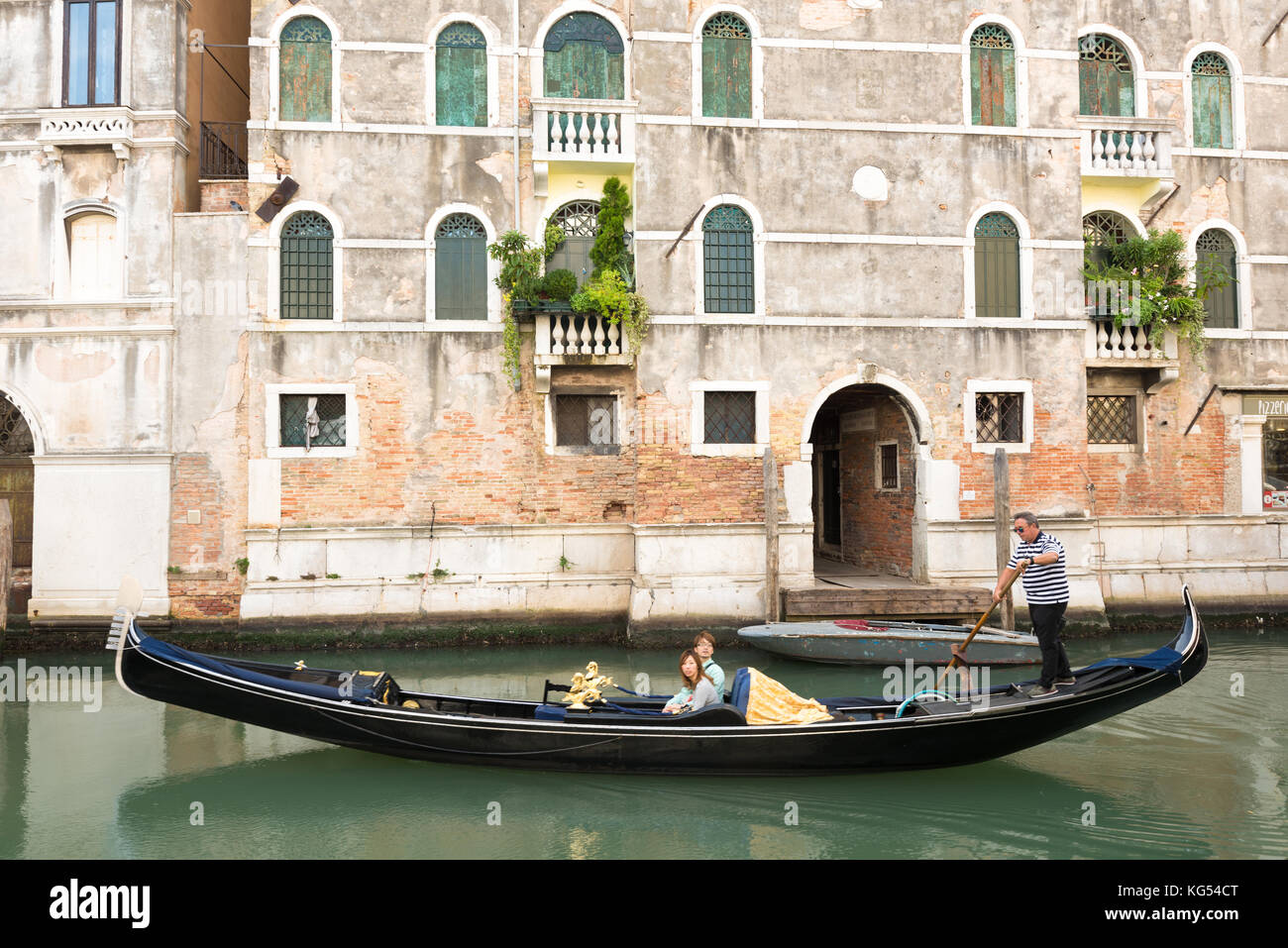 Gondoliere veneziano che punta la gondola attraverso le verdi acque dei canali di Venezia, Italia Foto Stock