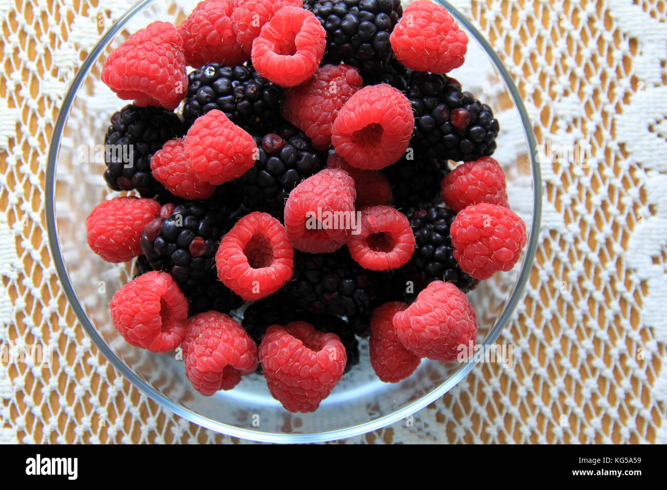 Grande ciotola di vetro riempita di frutta fresca di stagione posta su tovaglia graziosa del pizzo è una colazione tentante per la gente che cerca di migliorare la loro salute. Foto Stock