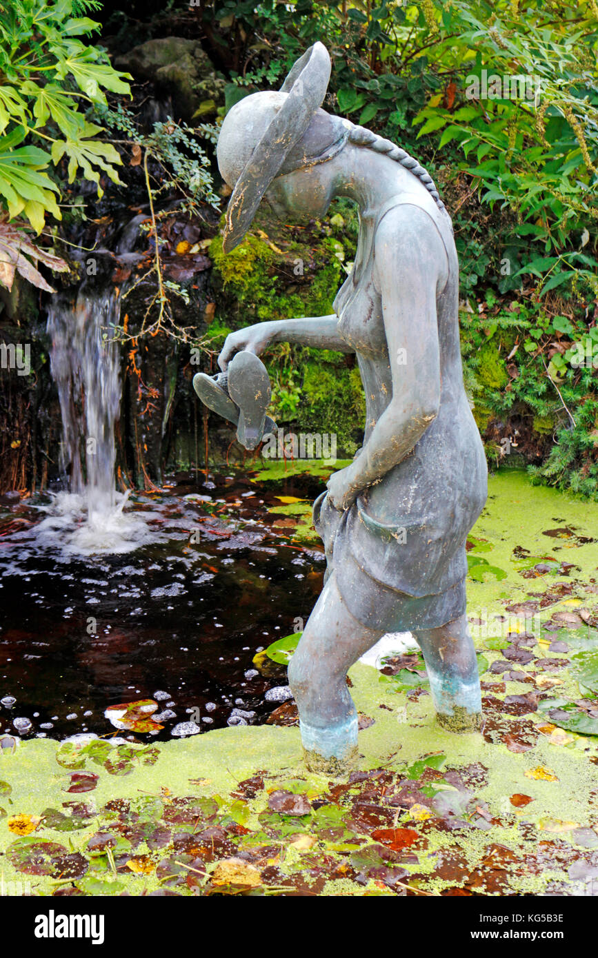 Un giardino dispongono di una piccola cascata e laghetto con una statua di una giovane ragazza guadare attraverso l'acqua. Foto Stock