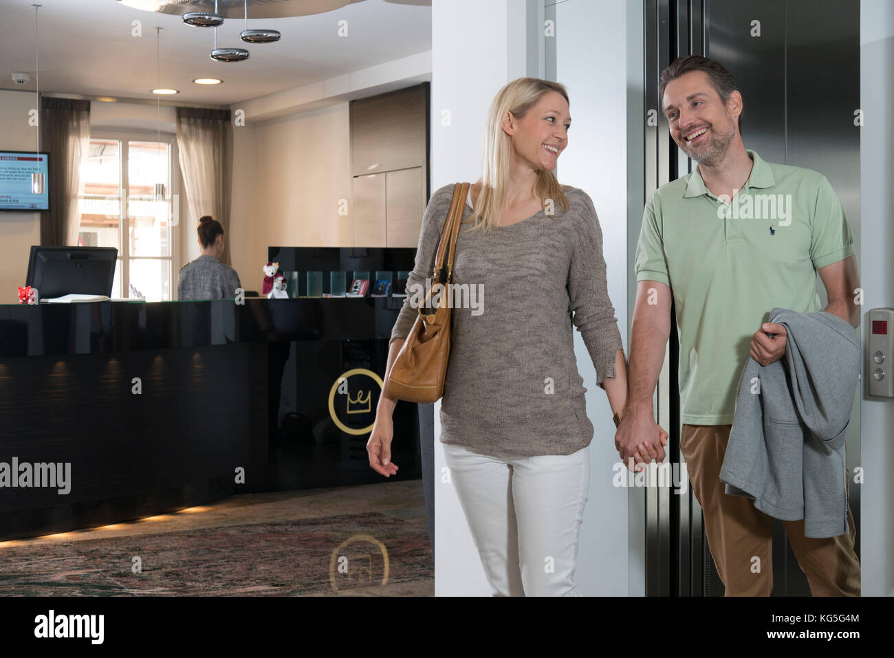 Coppia arriva laughingly fuori dell'ascensore in hotel, mano nella mano Foto Stock