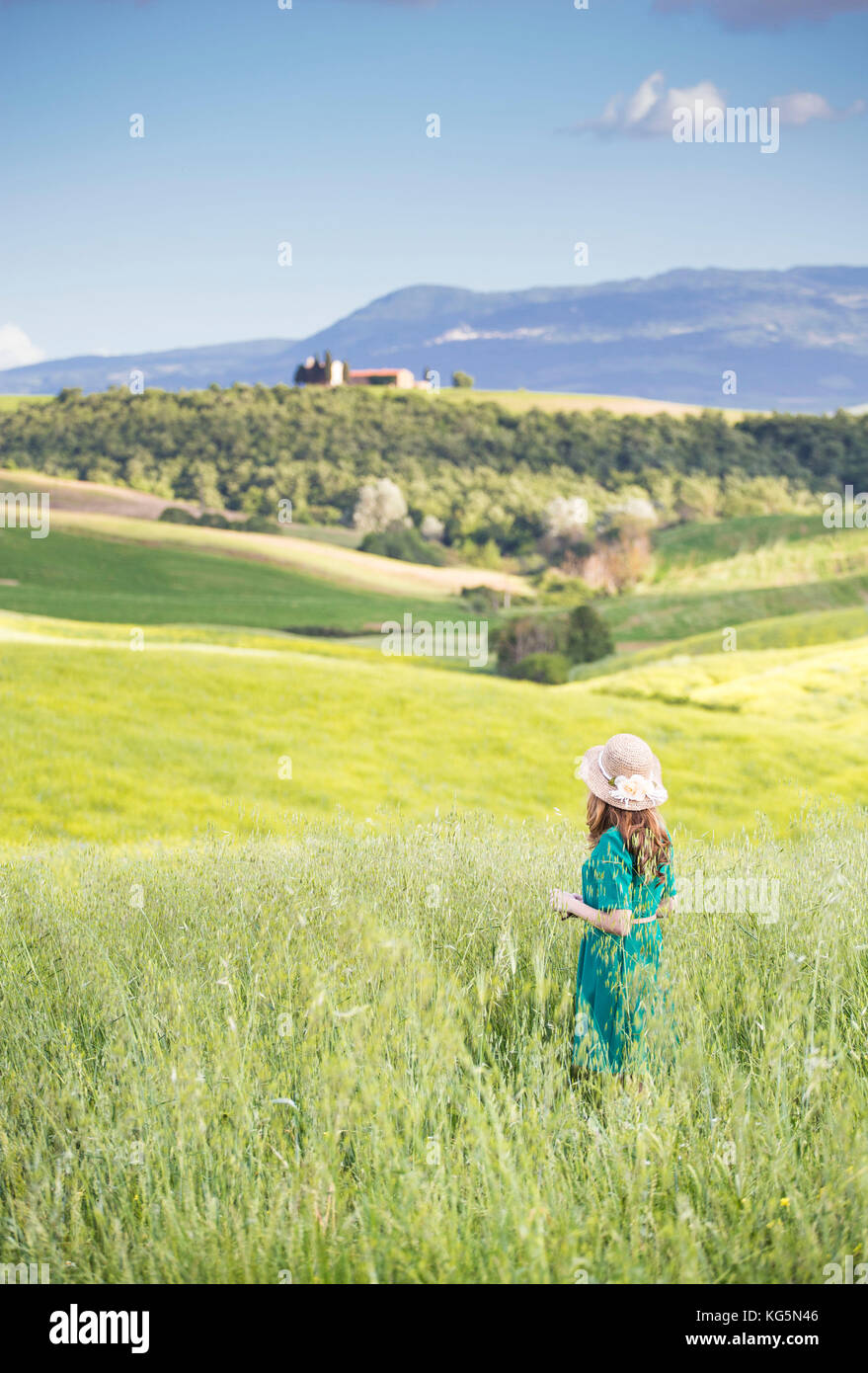 Una ragazza in un abito verde che cammina attraverso i campi dorati della Toscana. Val d'Orcia, Provincia di Siena, Toscana, Italia Foto Stock