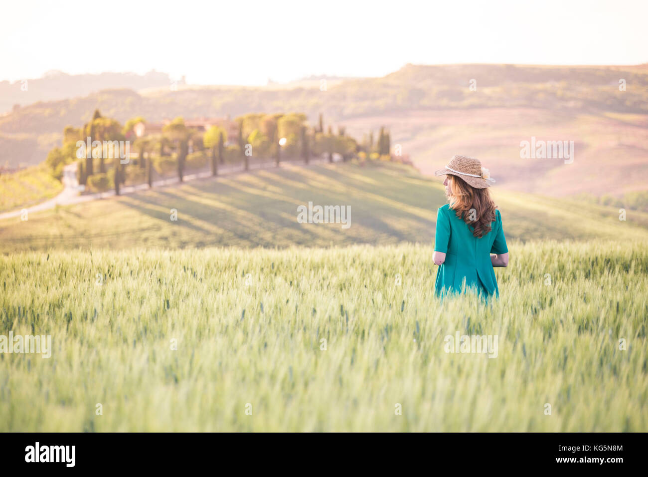 Una ragazza in un abito verde che cammina attraverso i campi dorati della Toscana. Val d'Orcia, Provincia di Siena, Toscana, Italia Foto Stock