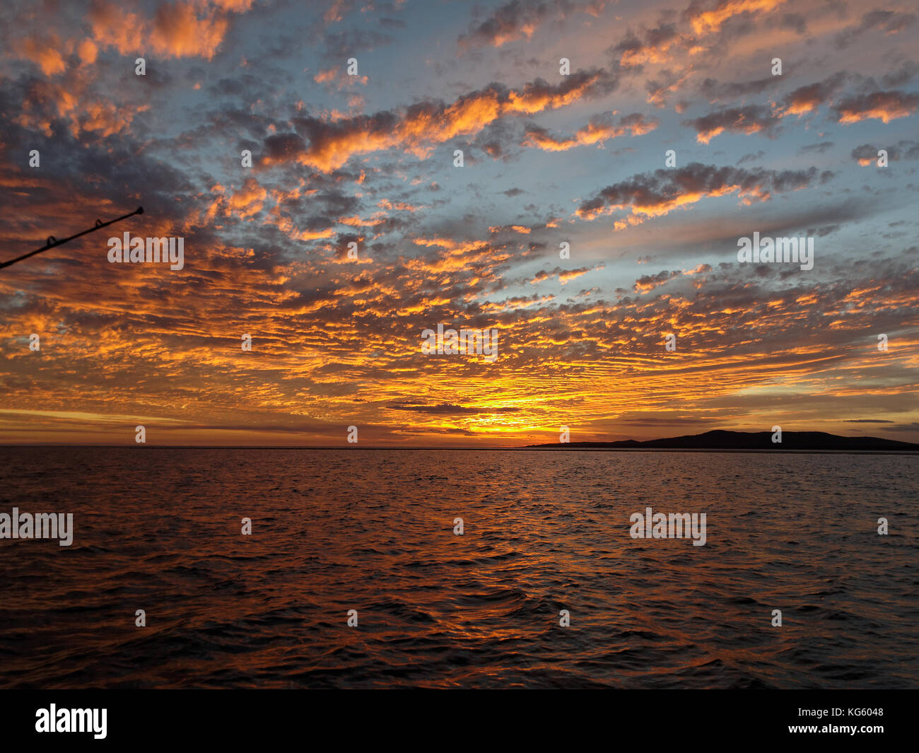 Un impressionante e ispiratore di colore arancione NUVOLOSO TRAMONTO seascape oltre l'acqua di mare con acqua riflessioni. Central Coast, Australia. Foto Stock