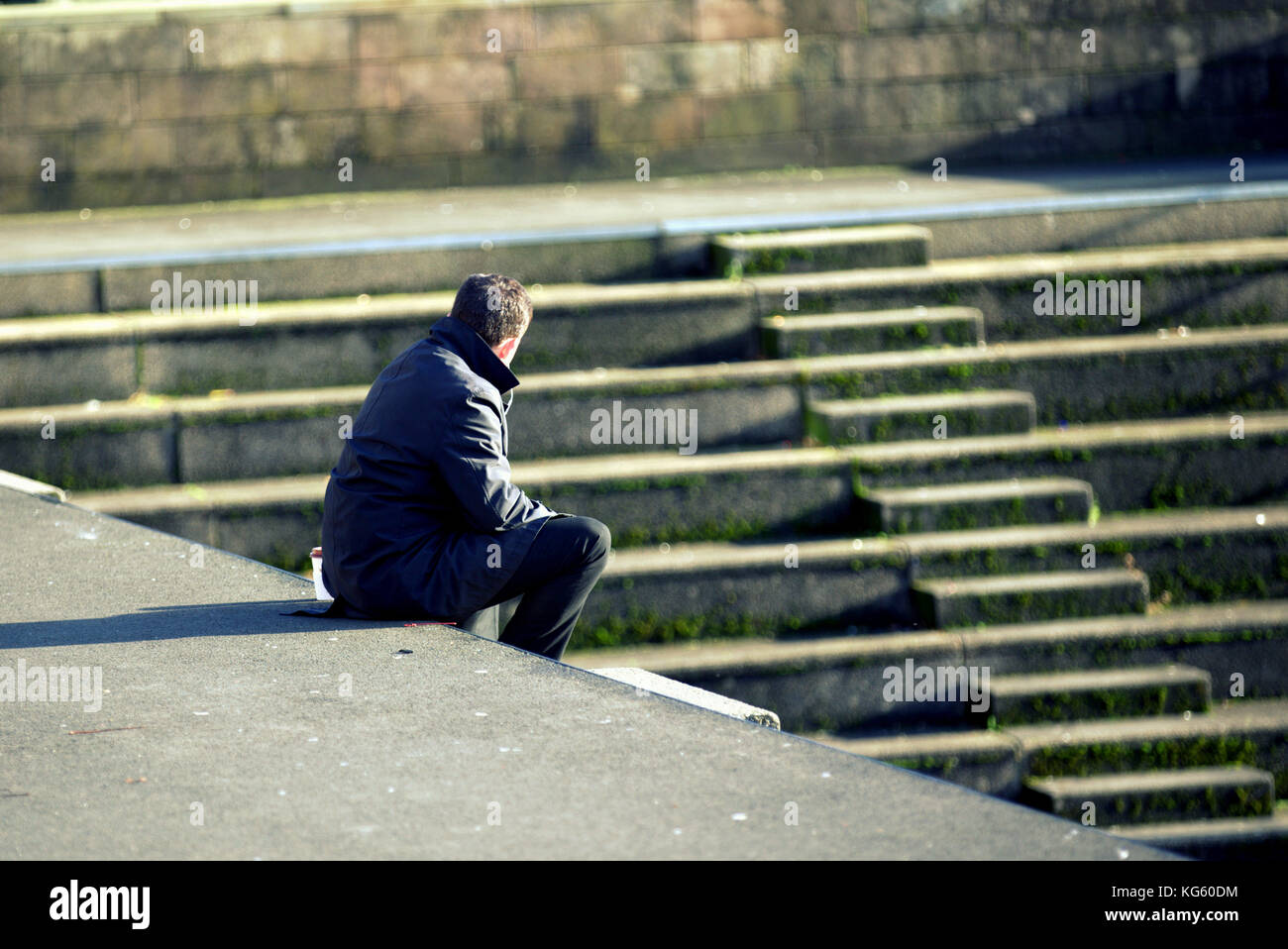 Singola bianco uomo solo contemplando pensando vicino a passi seduta sul gradino più basso della luce del sole Foto Stock