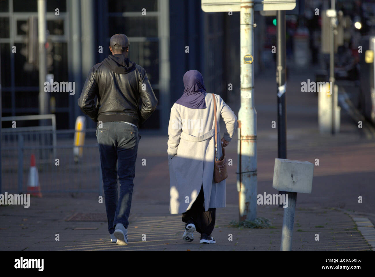 La famiglia asiatica rifugiata ha vestito la sciarpa Hijab per strada nel Regno Unito, un uomo e una donna di colore musulmana che camminavano per strada visti da dietro Foto Stock