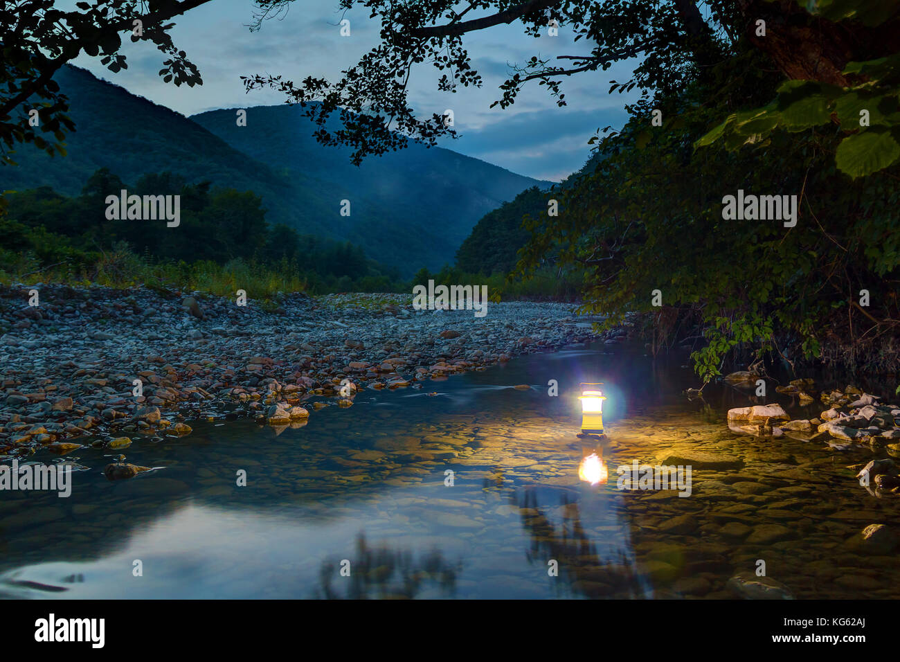 Luminosa lanterna a mano permanente sulla superficie del fiume makopse sullo sfondo della montagna tamyurdepe al crepuscolo, Sochi, Russia Foto Stock