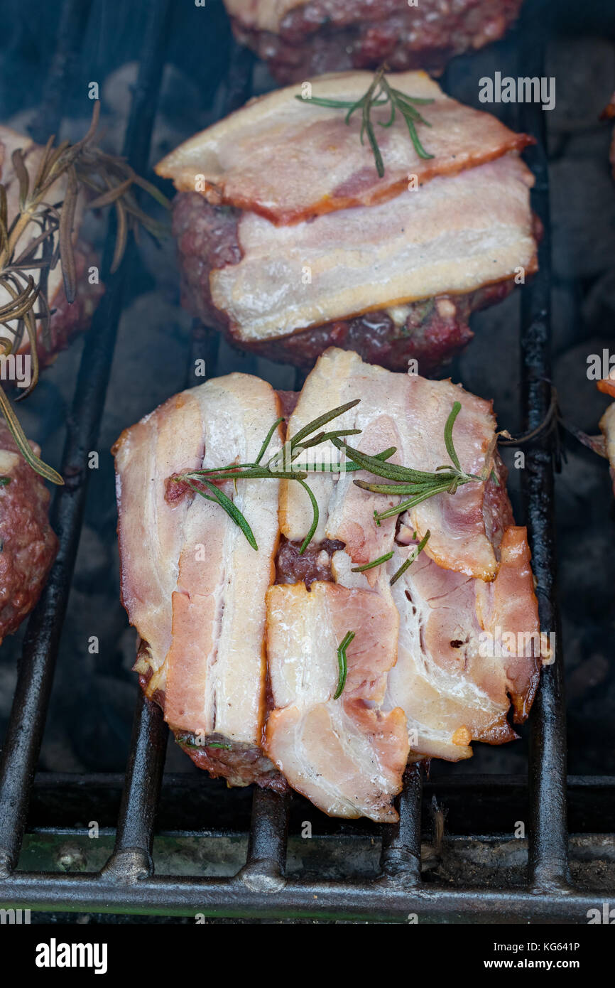 Hamburger con pancetta essendo grigliate sul barbecue Foto Stock