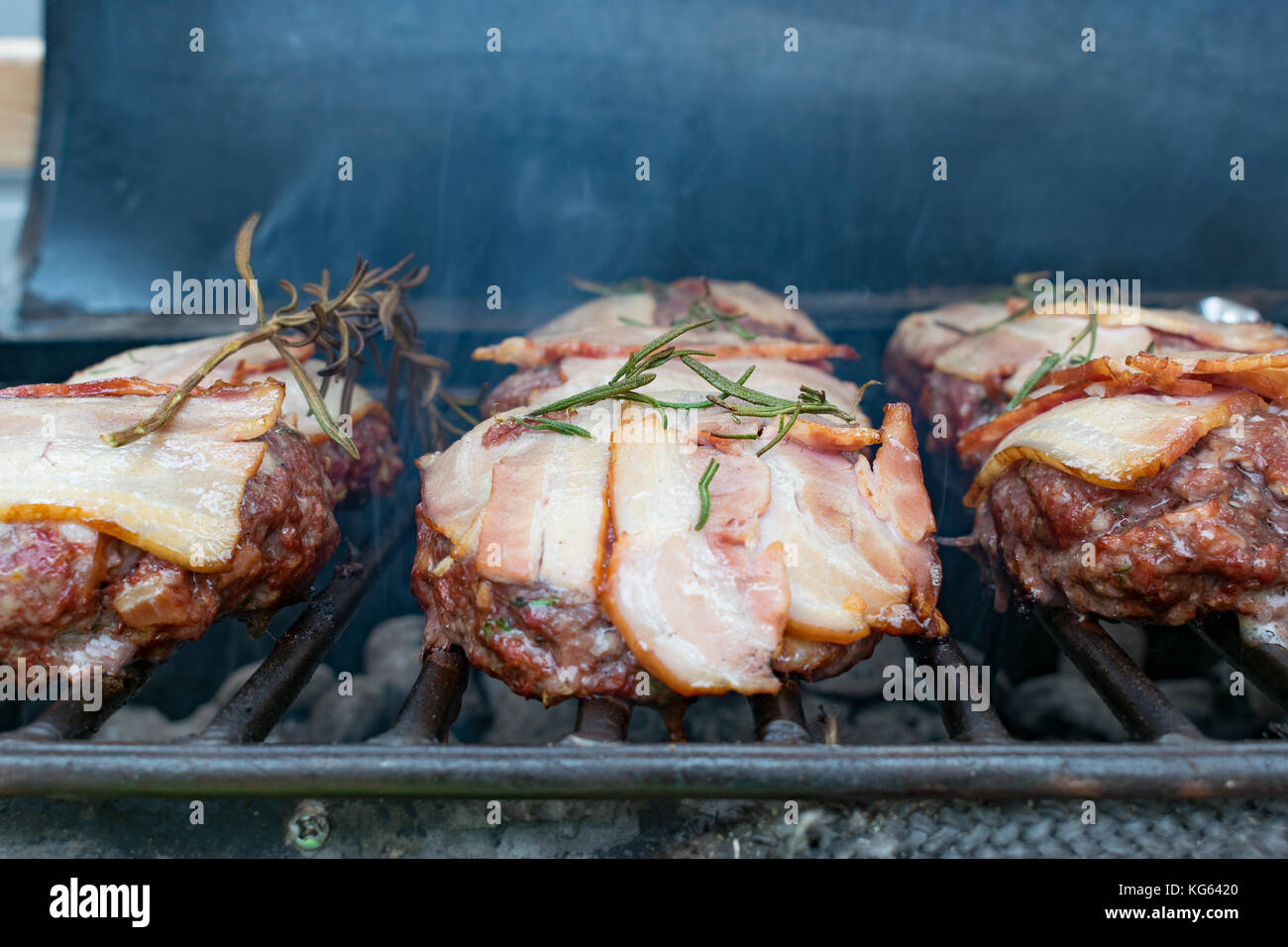 Hamburger con pancetta essendo grigliate sul barbecue Foto Stock