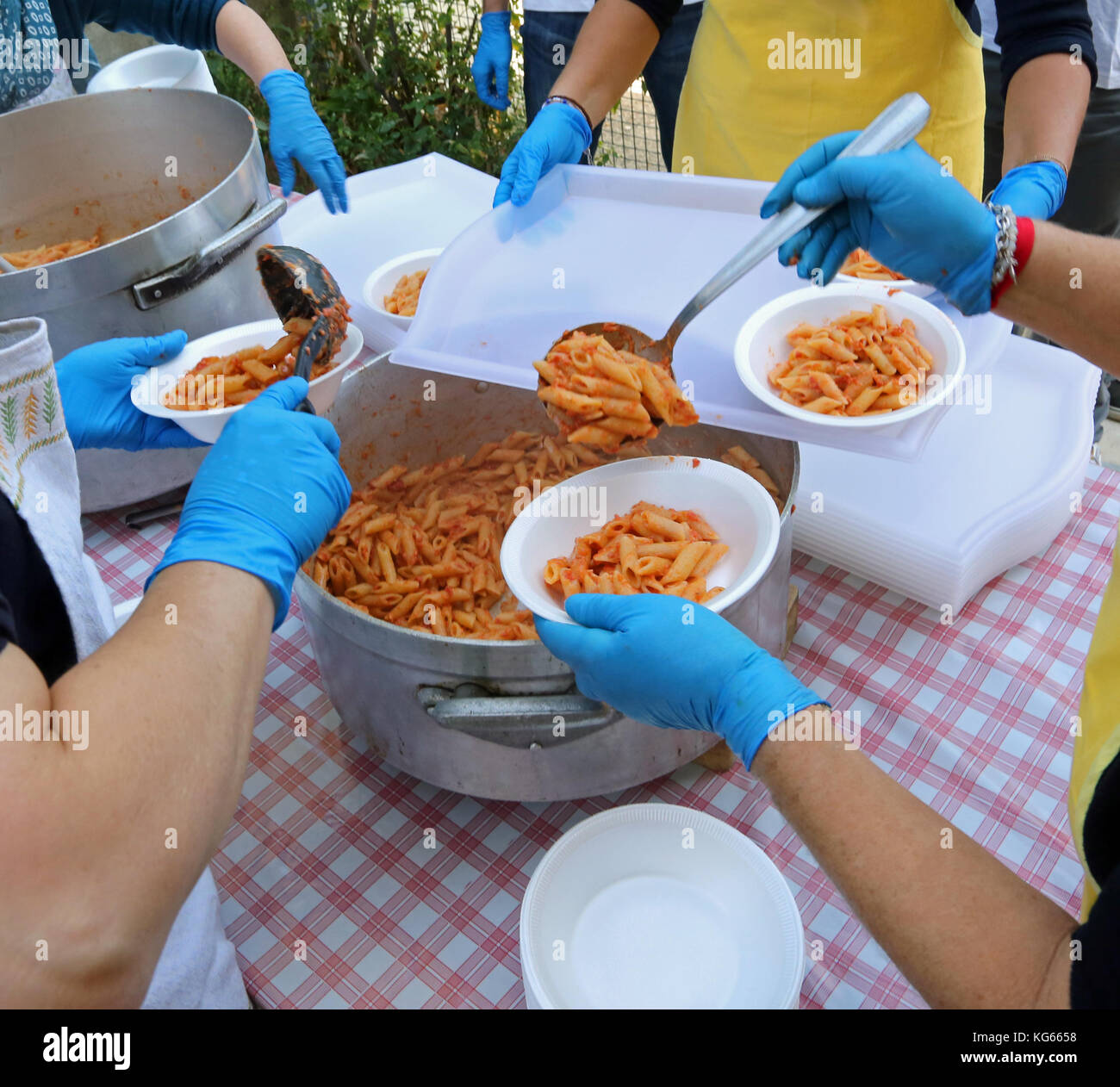 Le mani con guanti in lattice blu durante la distribuzione dei pasti con pasta e salsa di pomodoro in mensa Foto Stock