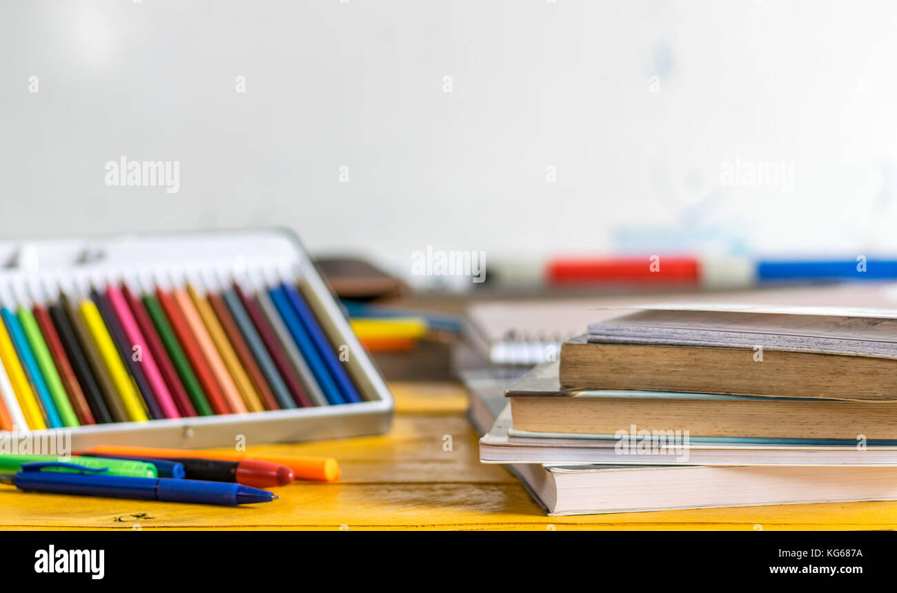 Matite colorate, penne e chiuso i libri e quaderni sulla parte superiore di un giallo tavolo in legno con una scuola di bianco scheda in background Foto Stock