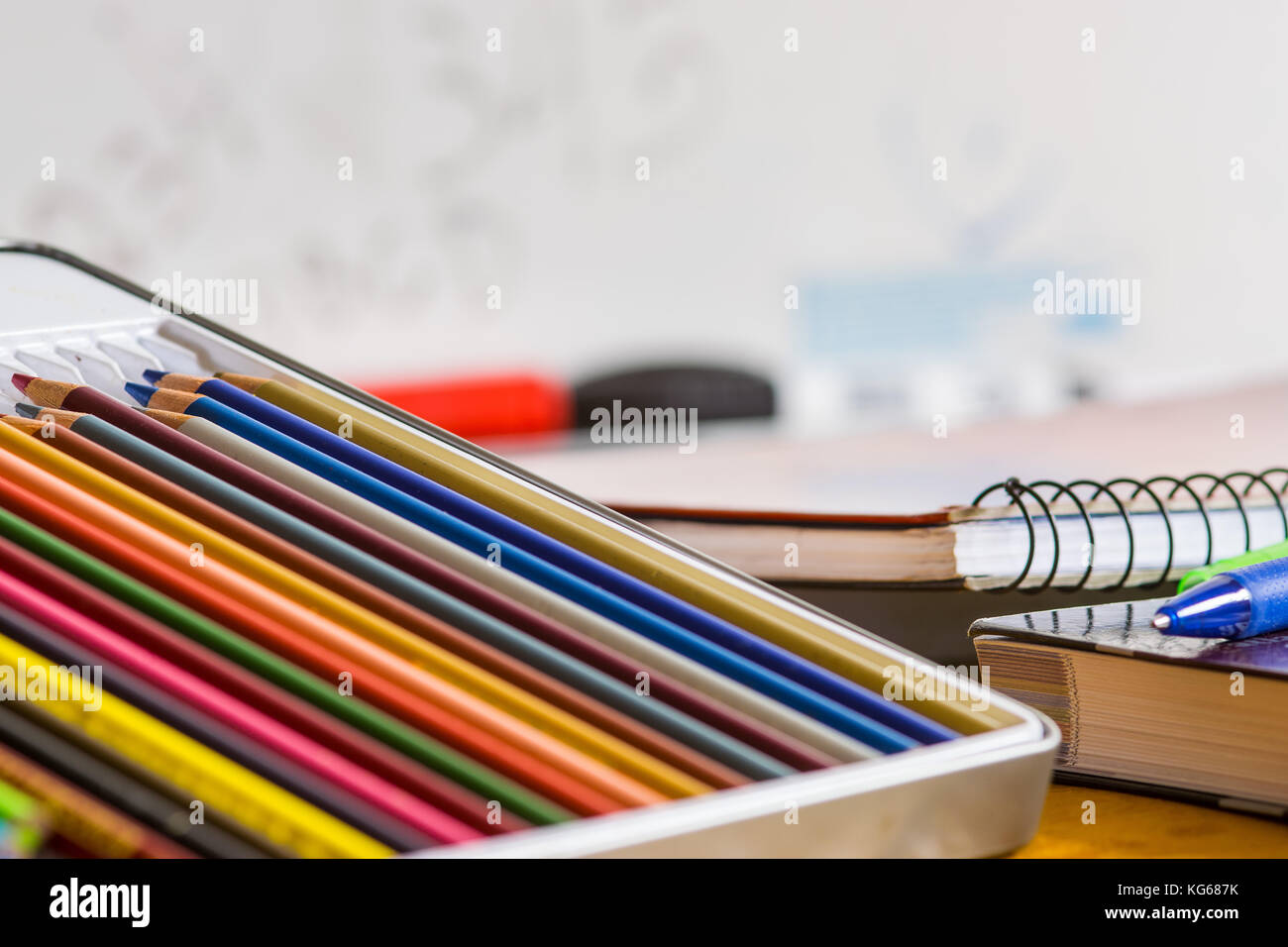 Matite colorate, penne e chiuso i libri e quaderni sulla parte superiore di un giallo tavolo in legno con una scuola di bianco scheda in background Foto Stock