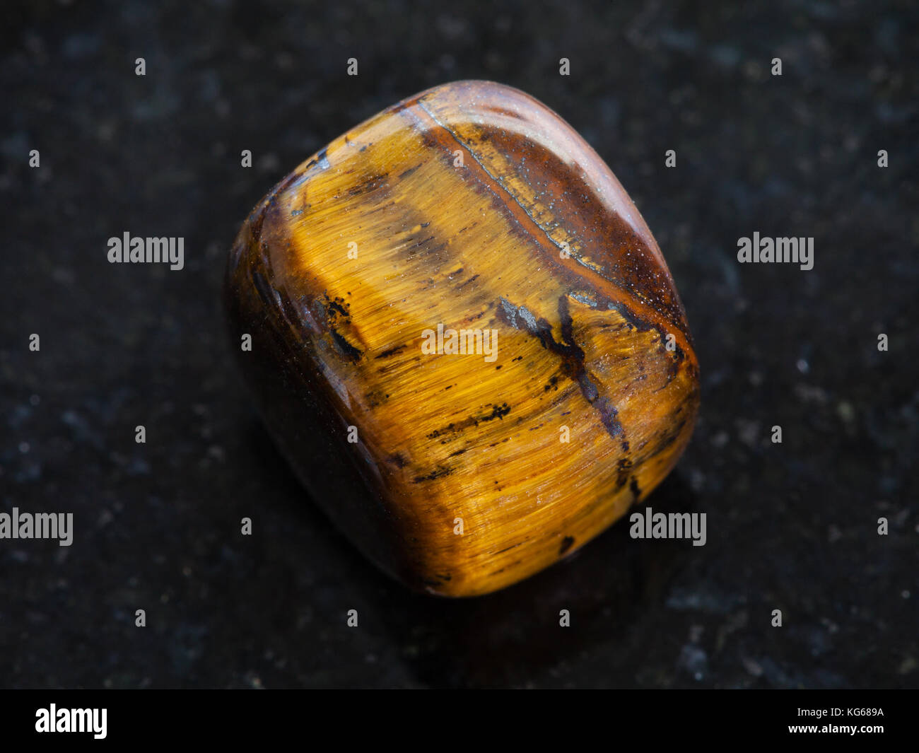 Le riprese in modalità macro di minerale naturale campione di roccia - lucidato occhio di tigre pietra preziosa sul granito scuro dello sfondo Foto Stock